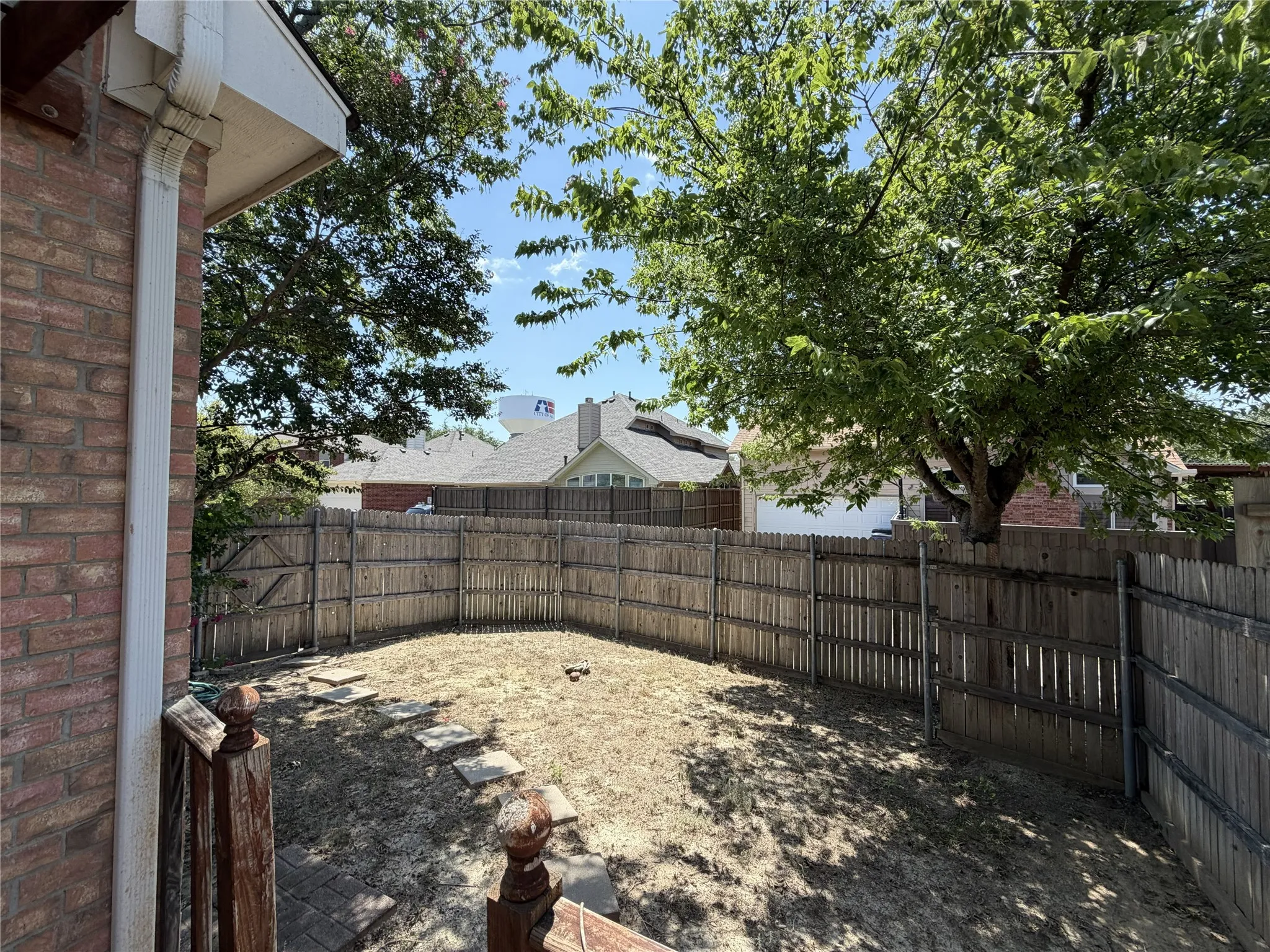 Enclosed backyard with wood privacy fencing, mature trees, and stone stepping path