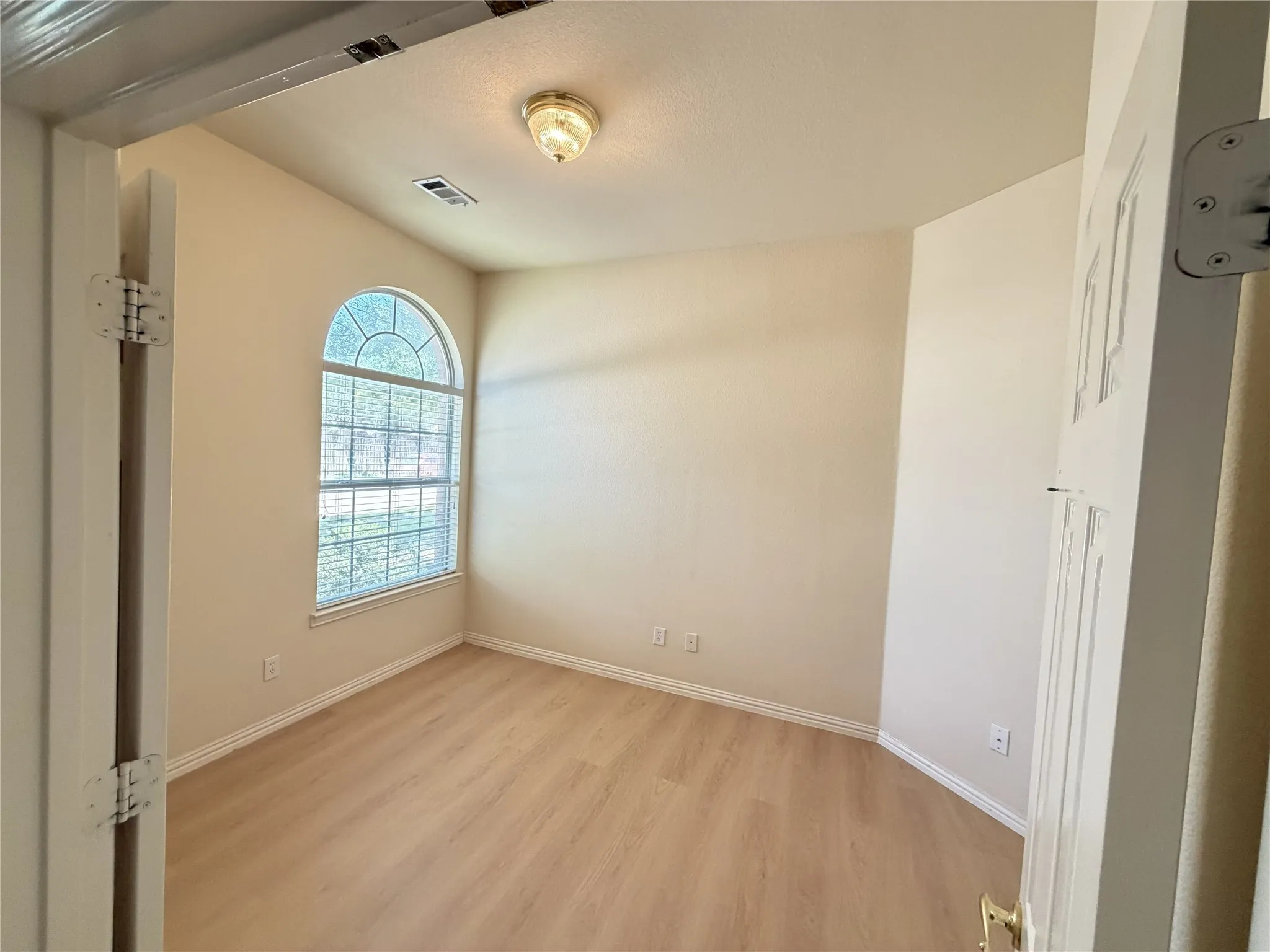Room featuring an arched window with blinds, wood-finish flooring, and white baseboards