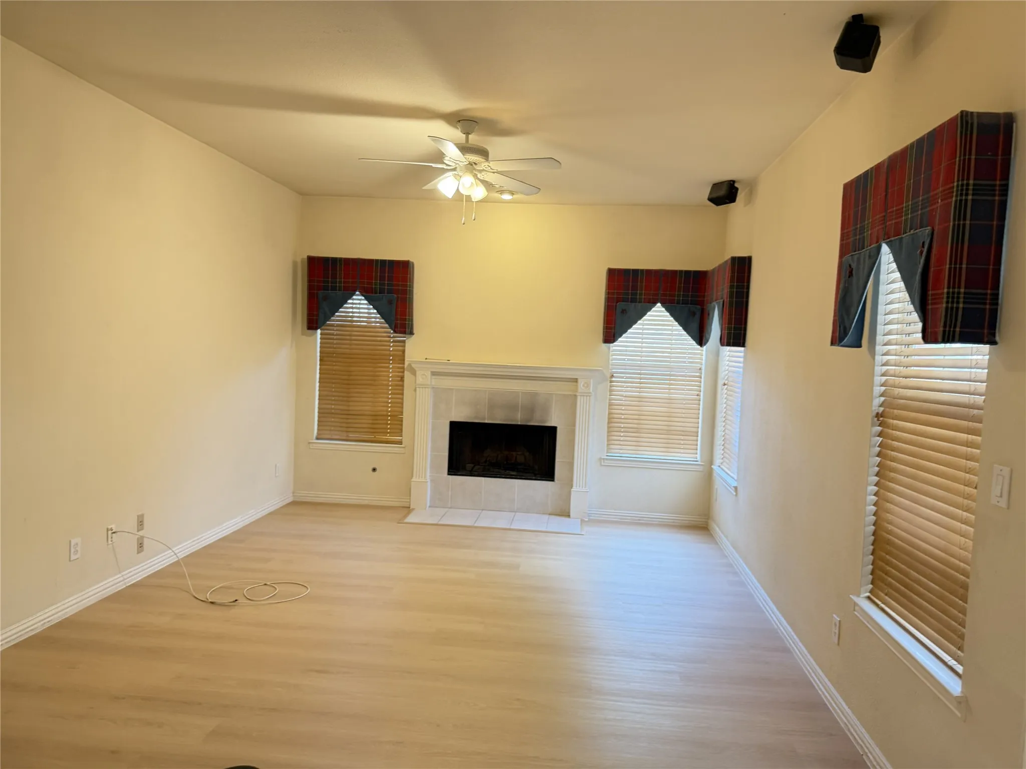 Living area featuring light wood-finish flooring, a central fireplace with a tile surround and mantel, and multiple windows with horizontal blinds