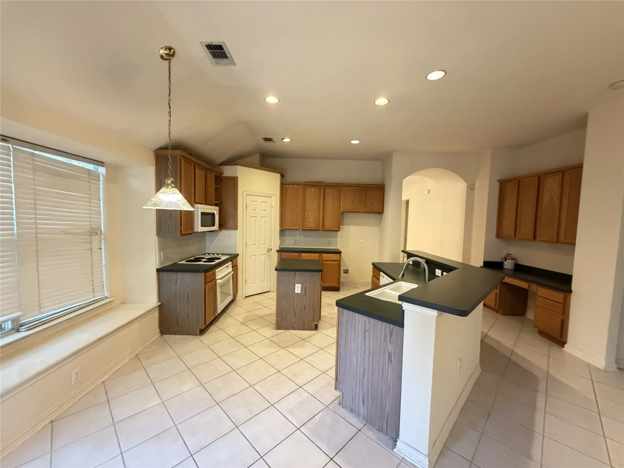 Spacious kitchen featuring extensive wood cabinetry, an integrated breakfast bar, a built-in microwave, a black electric cooktop, and a double basin sink