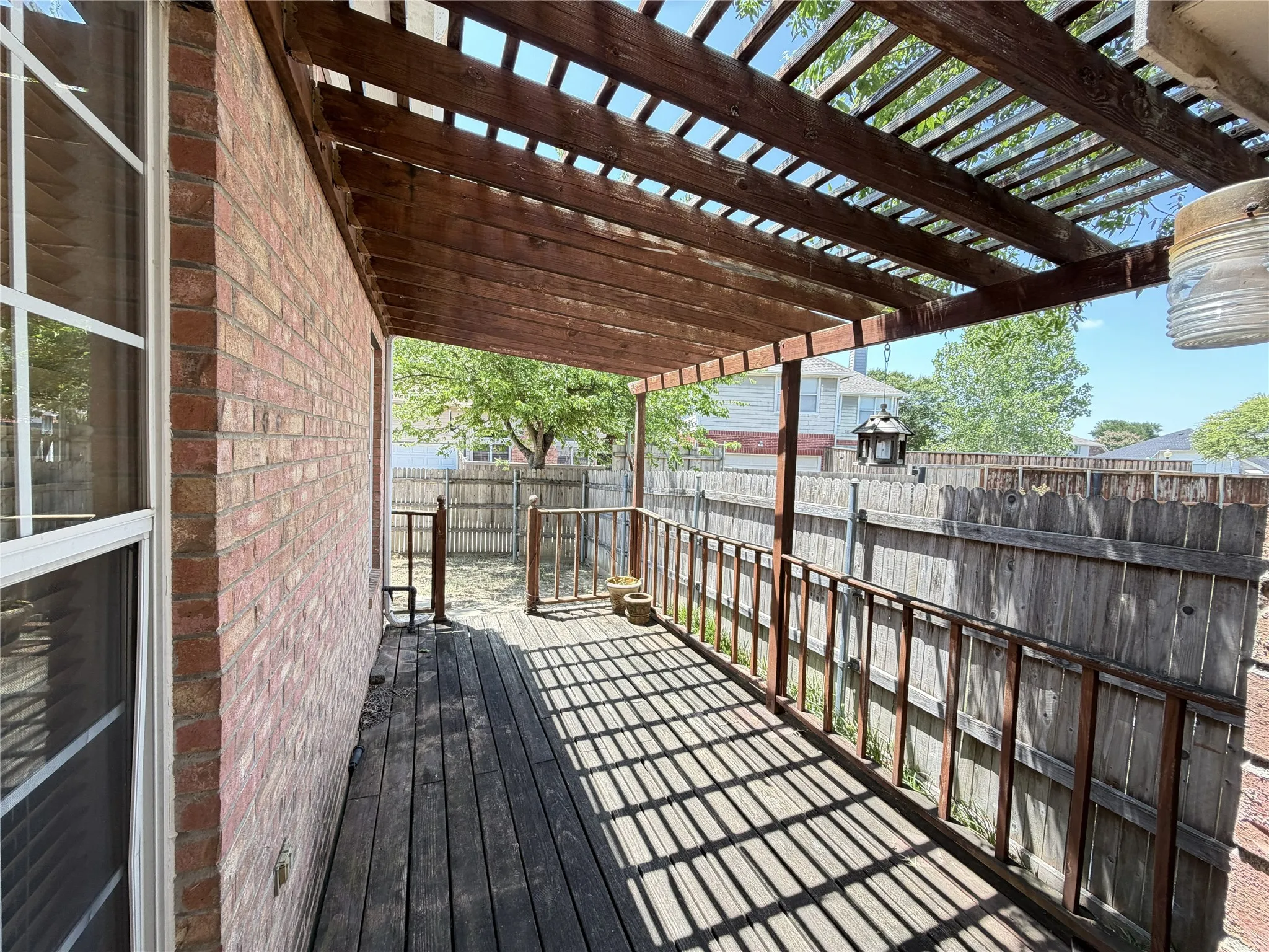 Covered wood deck featuring a slatted wood pergola, wood railing, and brick exterior wall