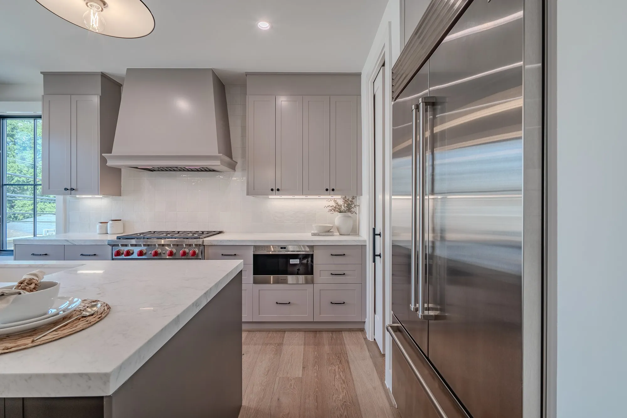 Kitchen featuring appliances with stainless steel finishes, wall chimney range hood, tasteful backsplash, light wood-style floors, and light stone countertops