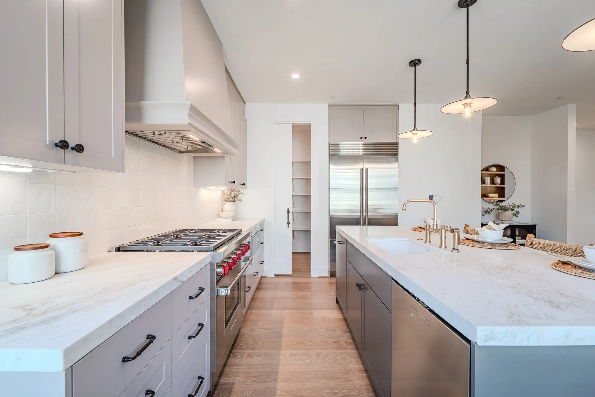 Kitchen featuring high end appliances, hanging light fixtures, gray cabinetry, an island with sink, and custom range hood