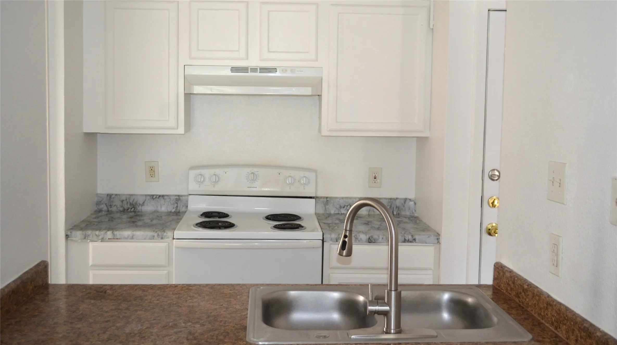 Kitchen featuring a double basin stainless steel sink with a high-arch faucet, white electric range with overhead ventilation, white cabinetry, and variegated countertops