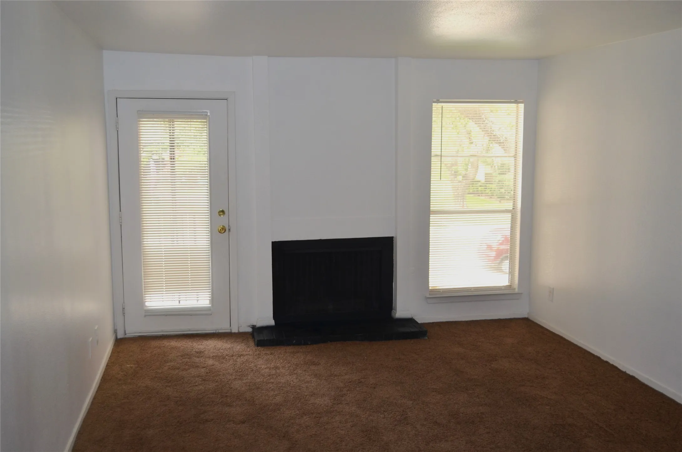 Living area featuring a fireplace, a glass-paneled door with integrated blinds, and a large window with blinds