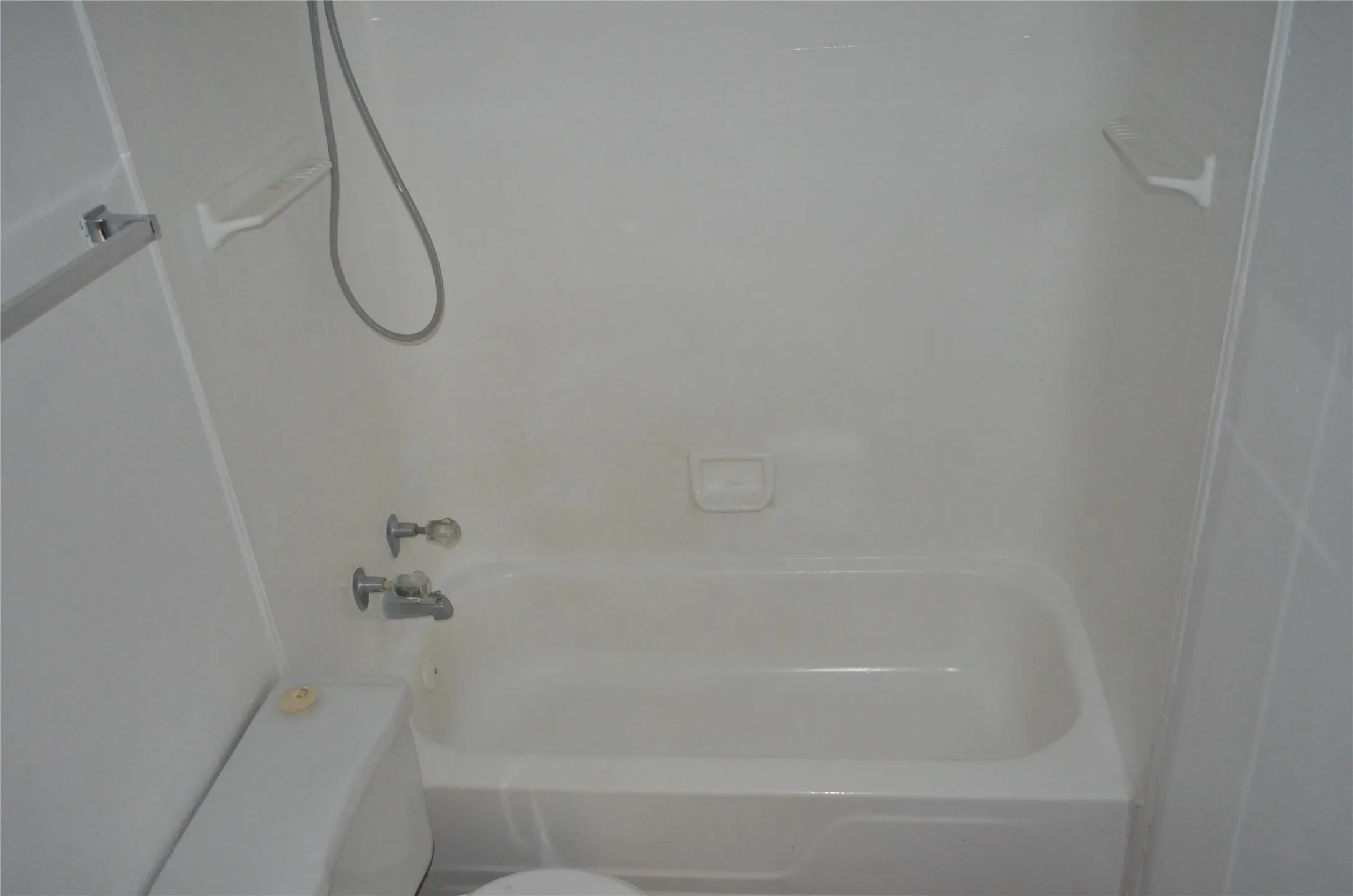 White bathtub with integrated shower, chrome fixtures, and a wall-mounted shower head with hose
