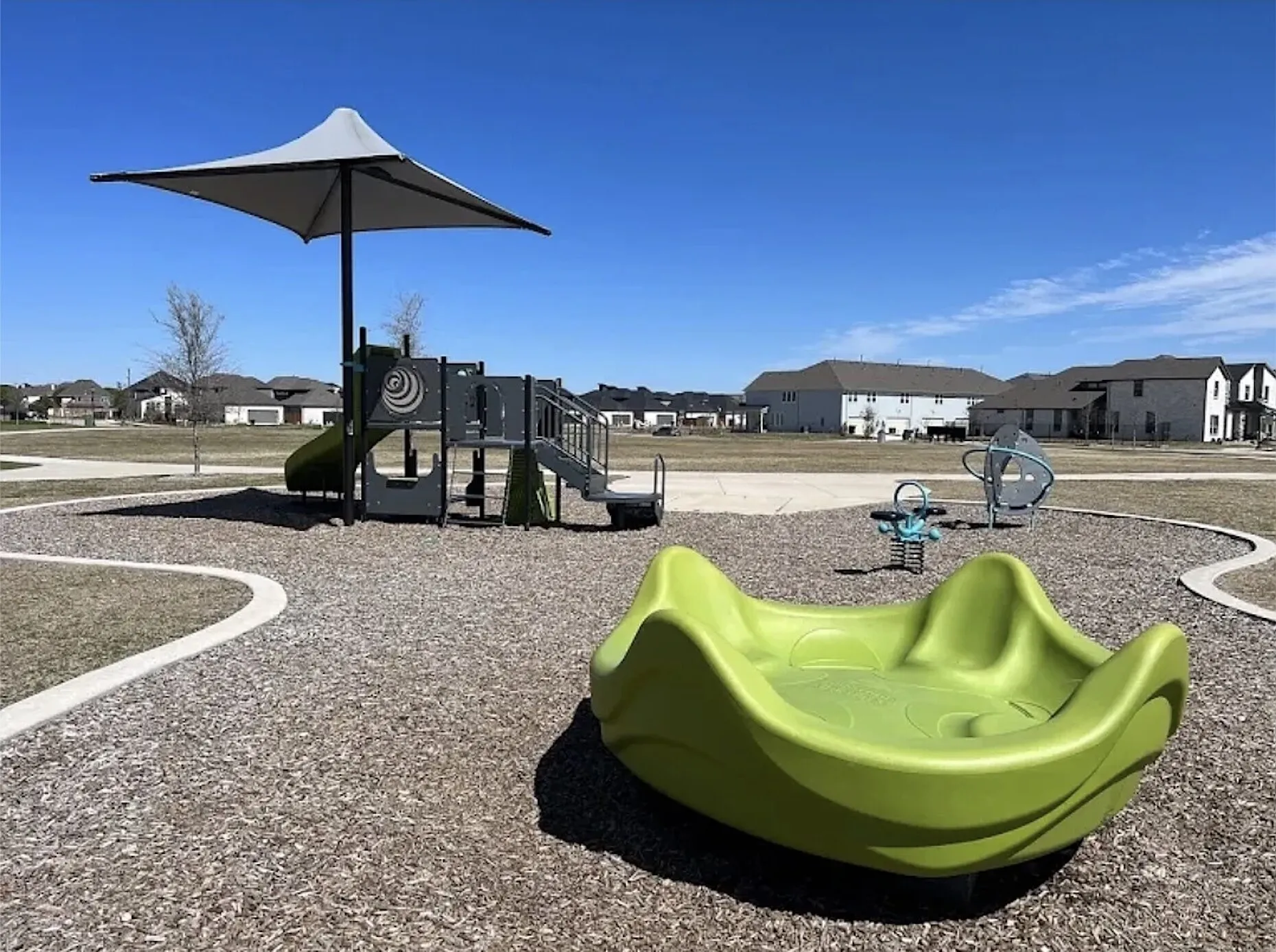 Community playground featuring modern play equipment, a protective shade structure, and a wood chip surface
