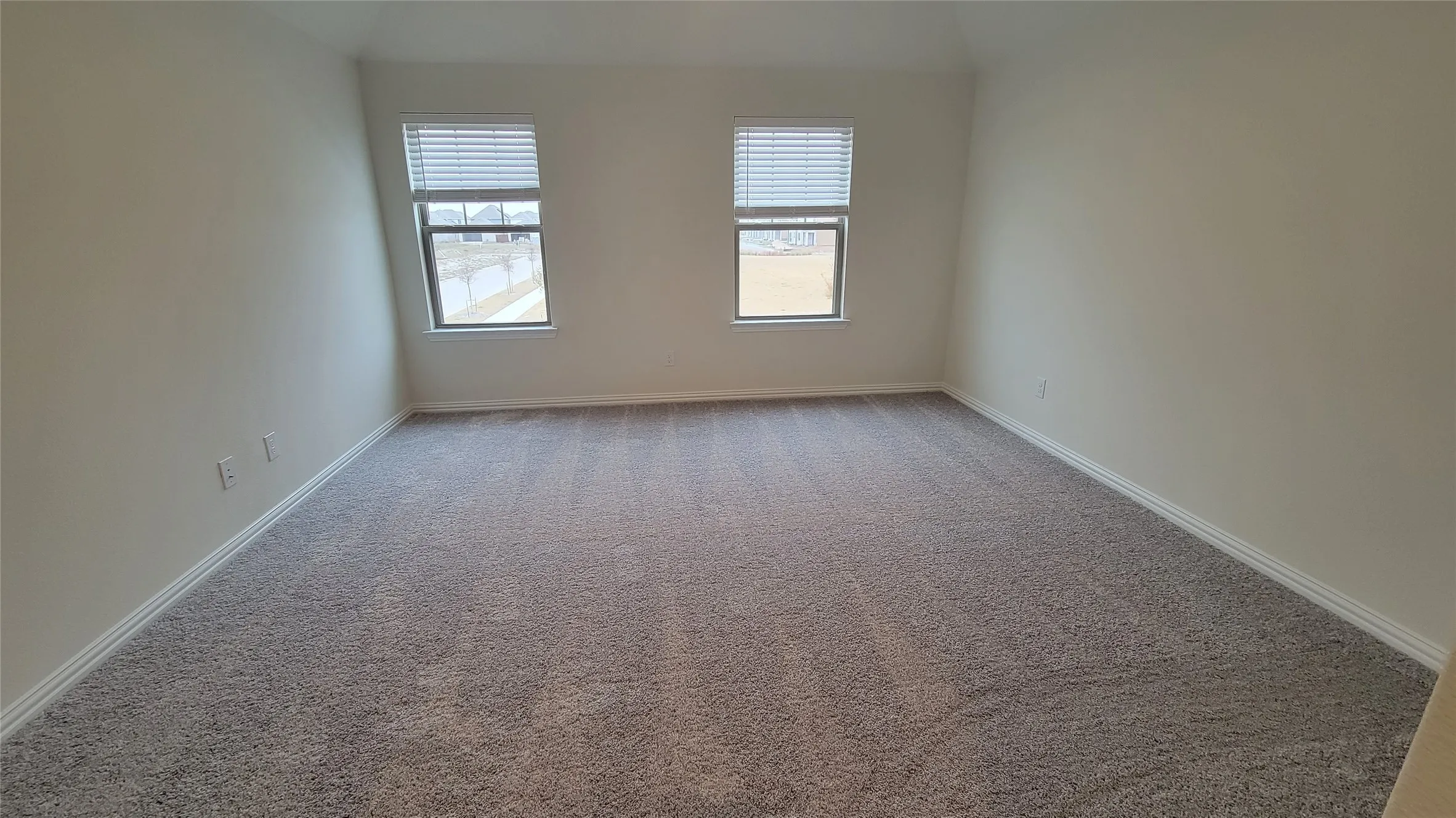 Spacious room featuring neutral wall paint, two windows with blinds, and light gray carpeting