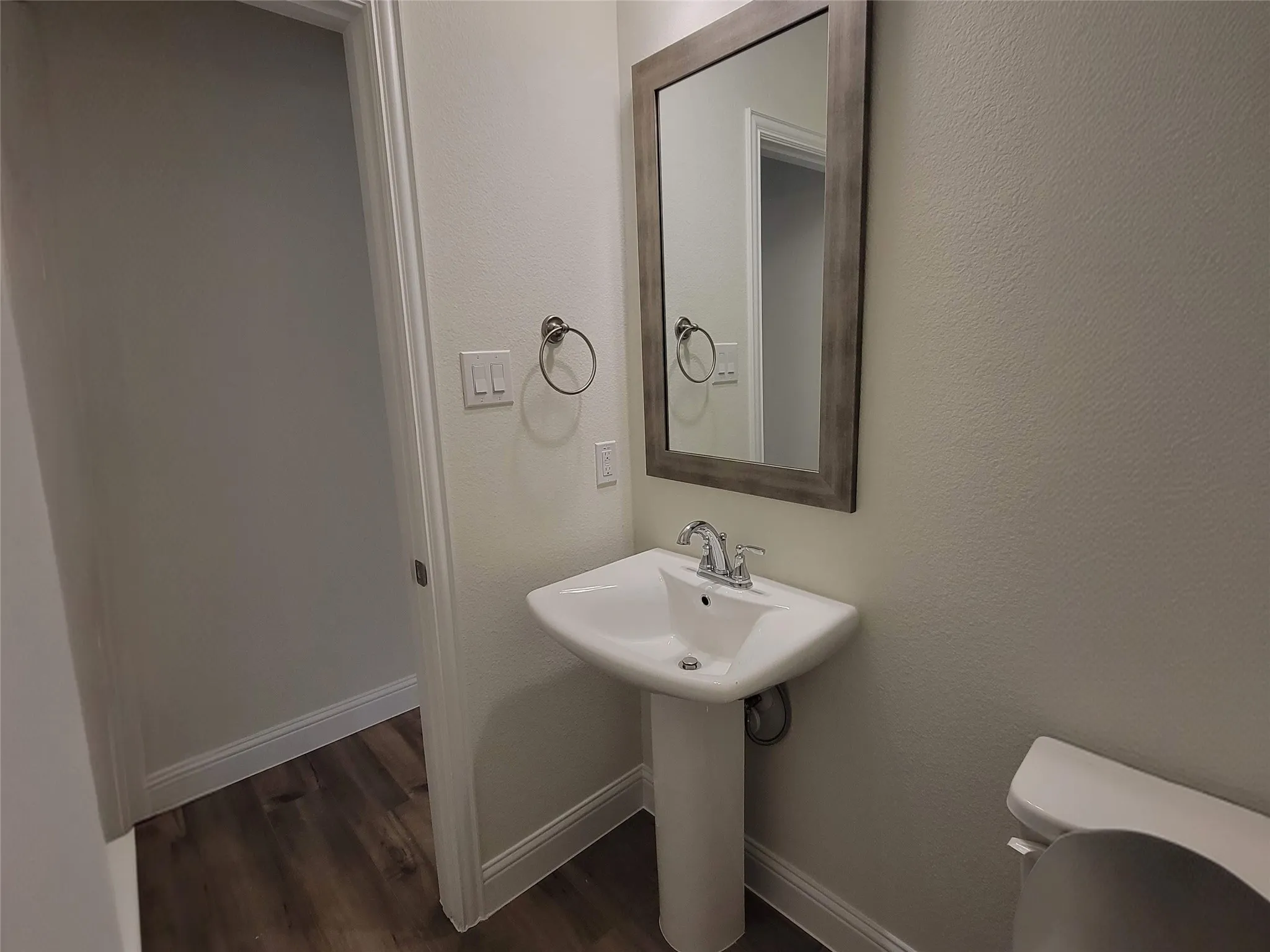 Pedestal sink with chrome faucet, framed mirror, and wood-finish flooring