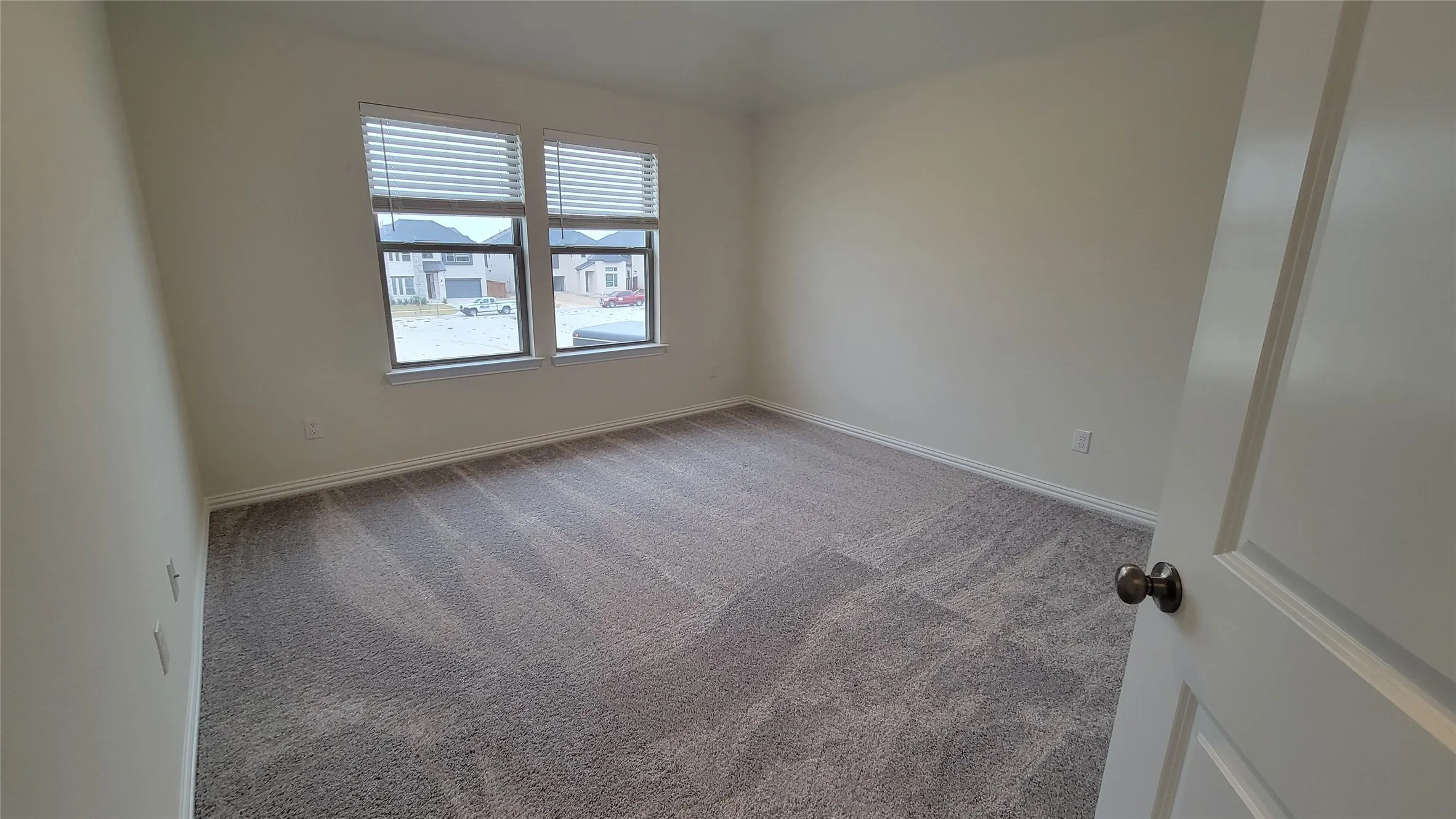Spacious room featuring neutral carpeting, light-toned walls, and twin windows with horizontal blinds
