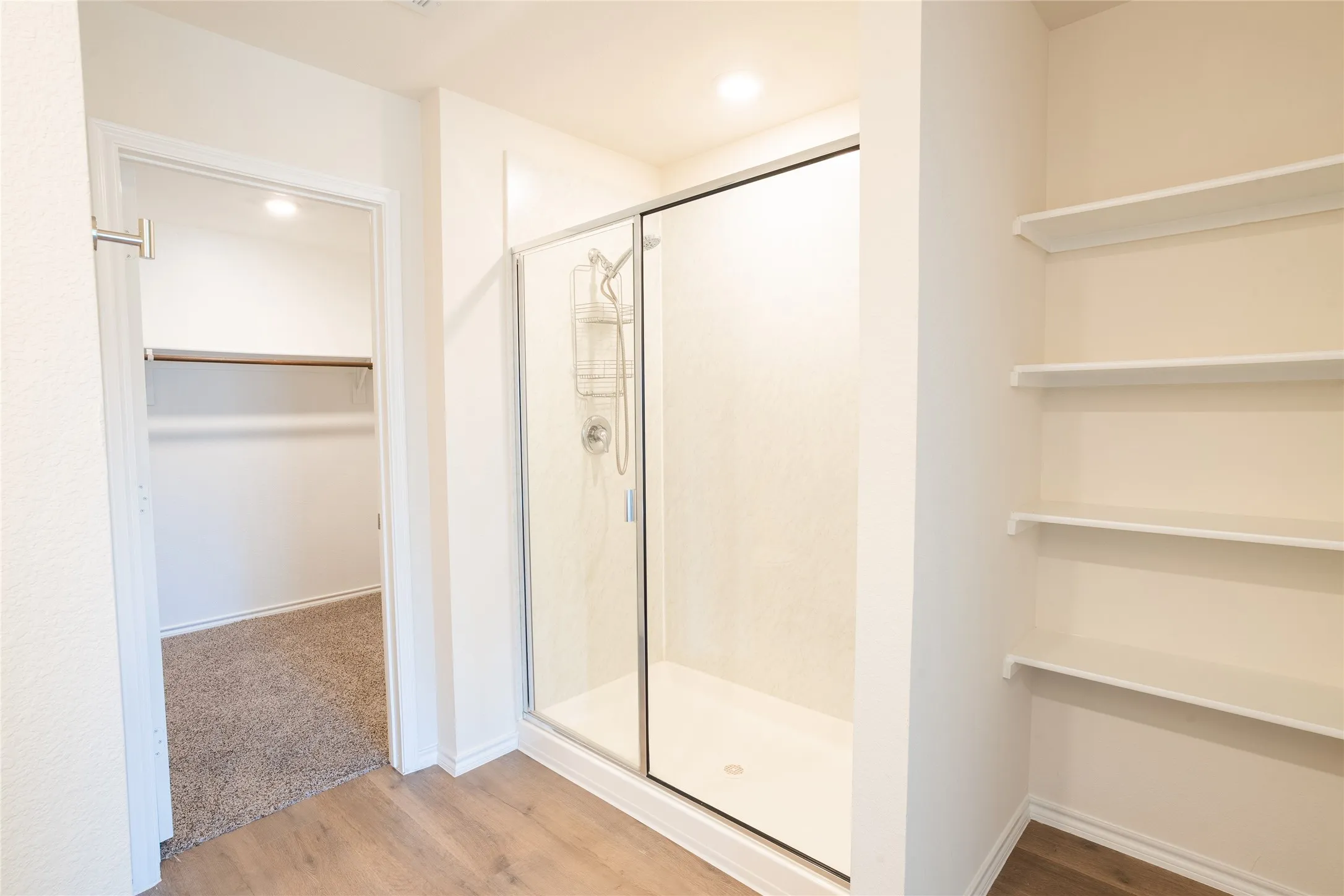 Master bathroom view of walk-in closet, glass shower, and open shelving