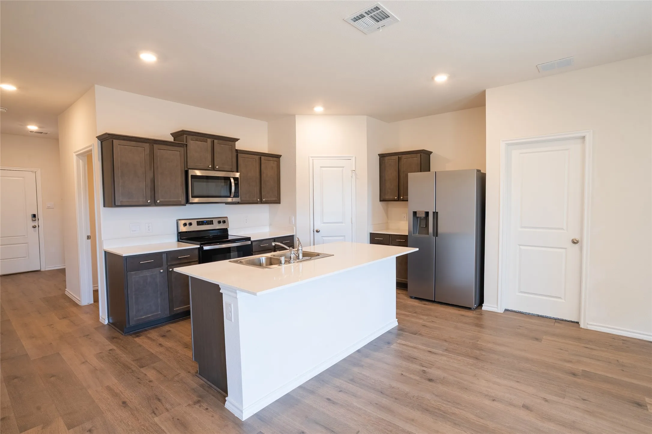 Kitchen featuring stainless steel appliances, fridge with water filter and ice maker, dark brown cabinetry, white counters, pantry, and wood finished floors