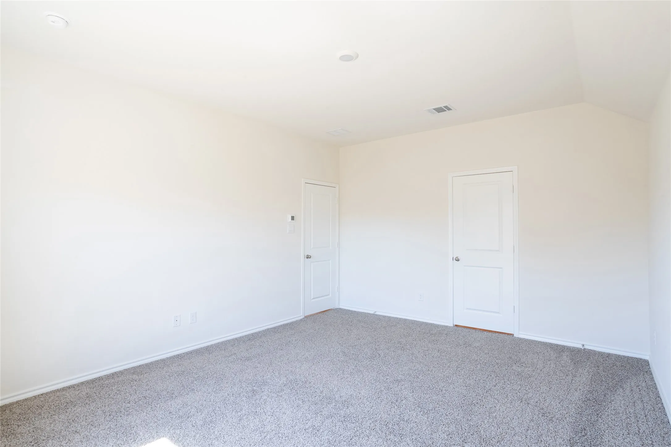 Carpeted master bedroom featuring lofted ceiling, bedroom door (left), and master bathroom door (right)