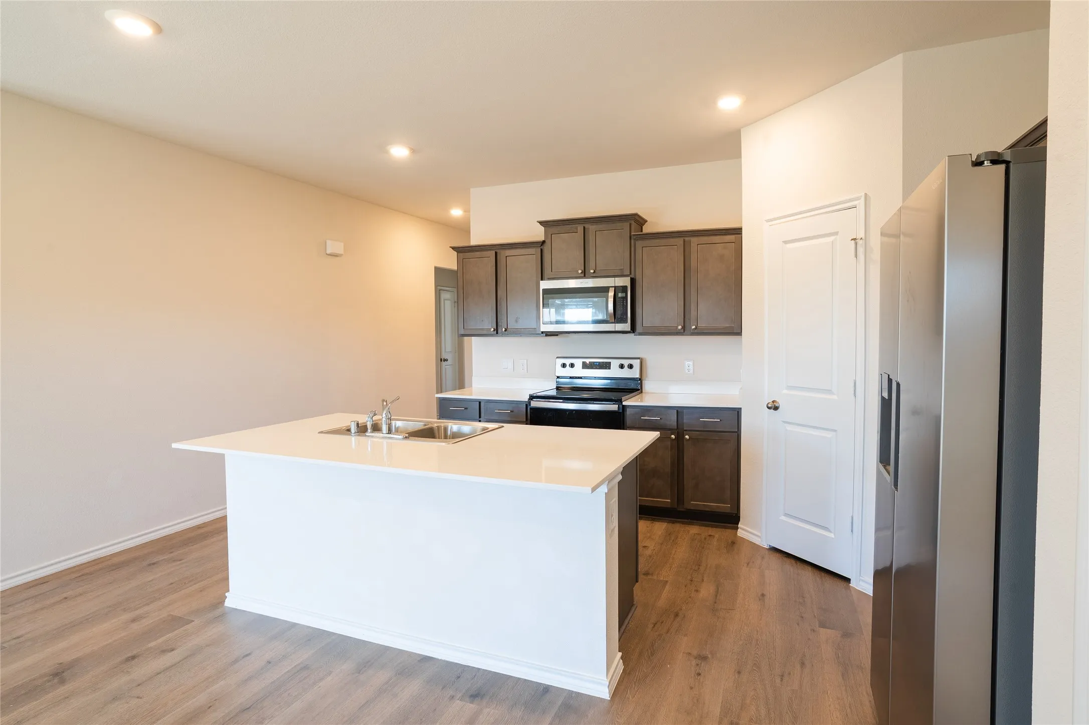 Kitchen featuring stainless steel appliances, fridge with water filter and ice maker, dark brown cabinetry, white counters, pantry, and wood finished floors