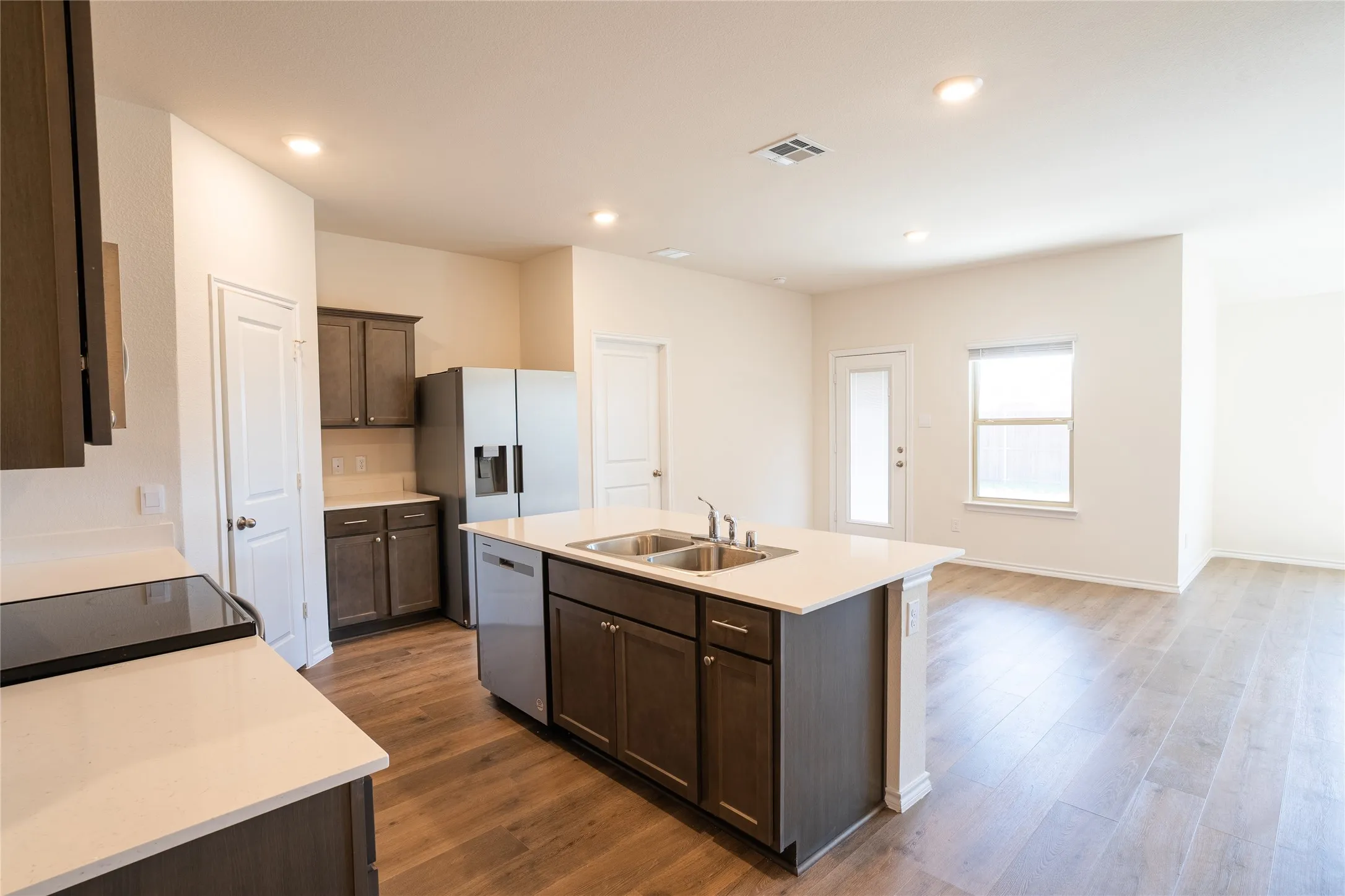 Kitchen featuring stainless steel appliances, fridge with water filter and ice maker, dark brown cabinetry, white counters, pantry, and wood finished floors