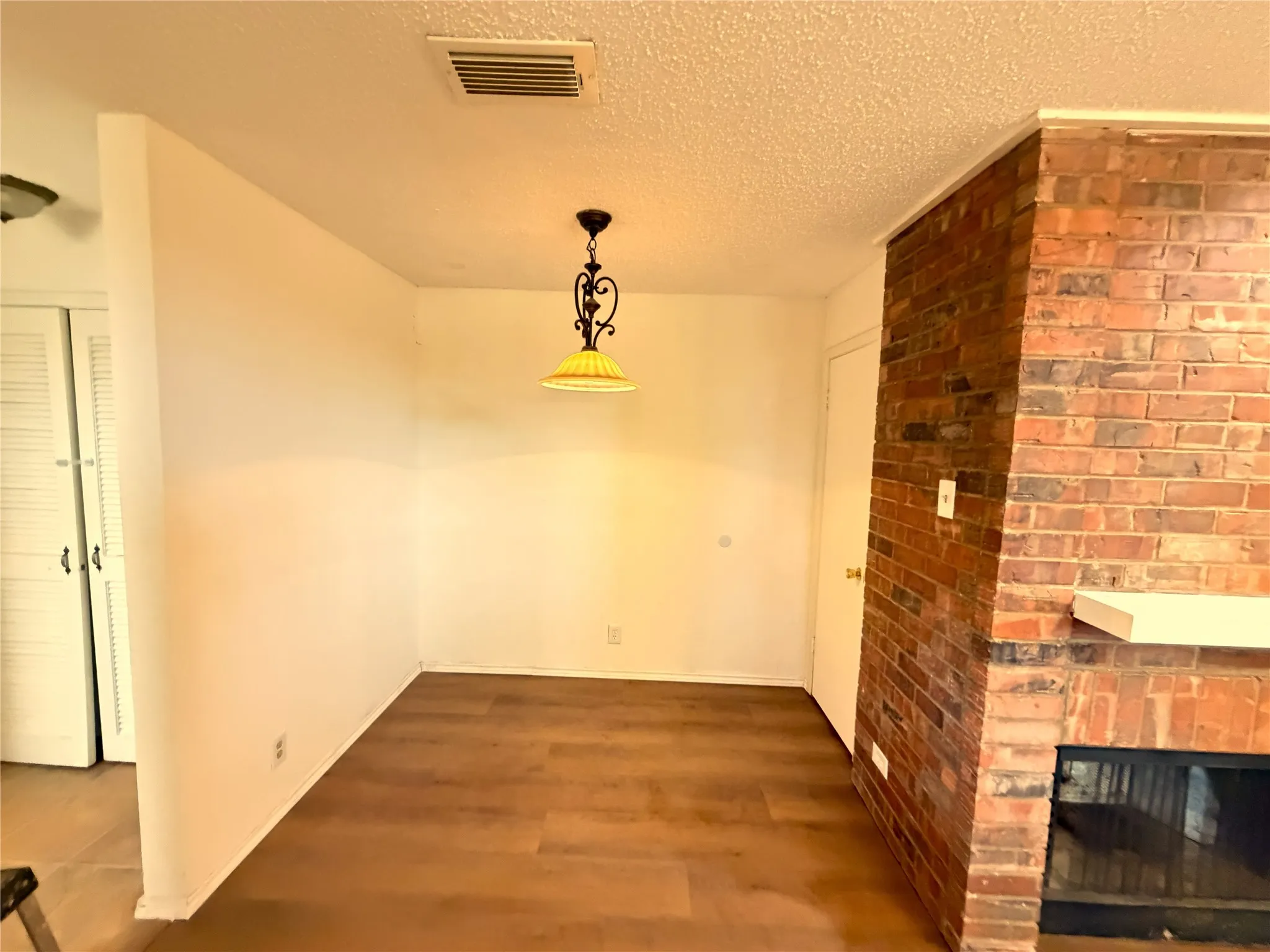 Interior space featuring wood-finish flooring, a brick fireplace with a white mantel, and a ceiling-mounted light fixture