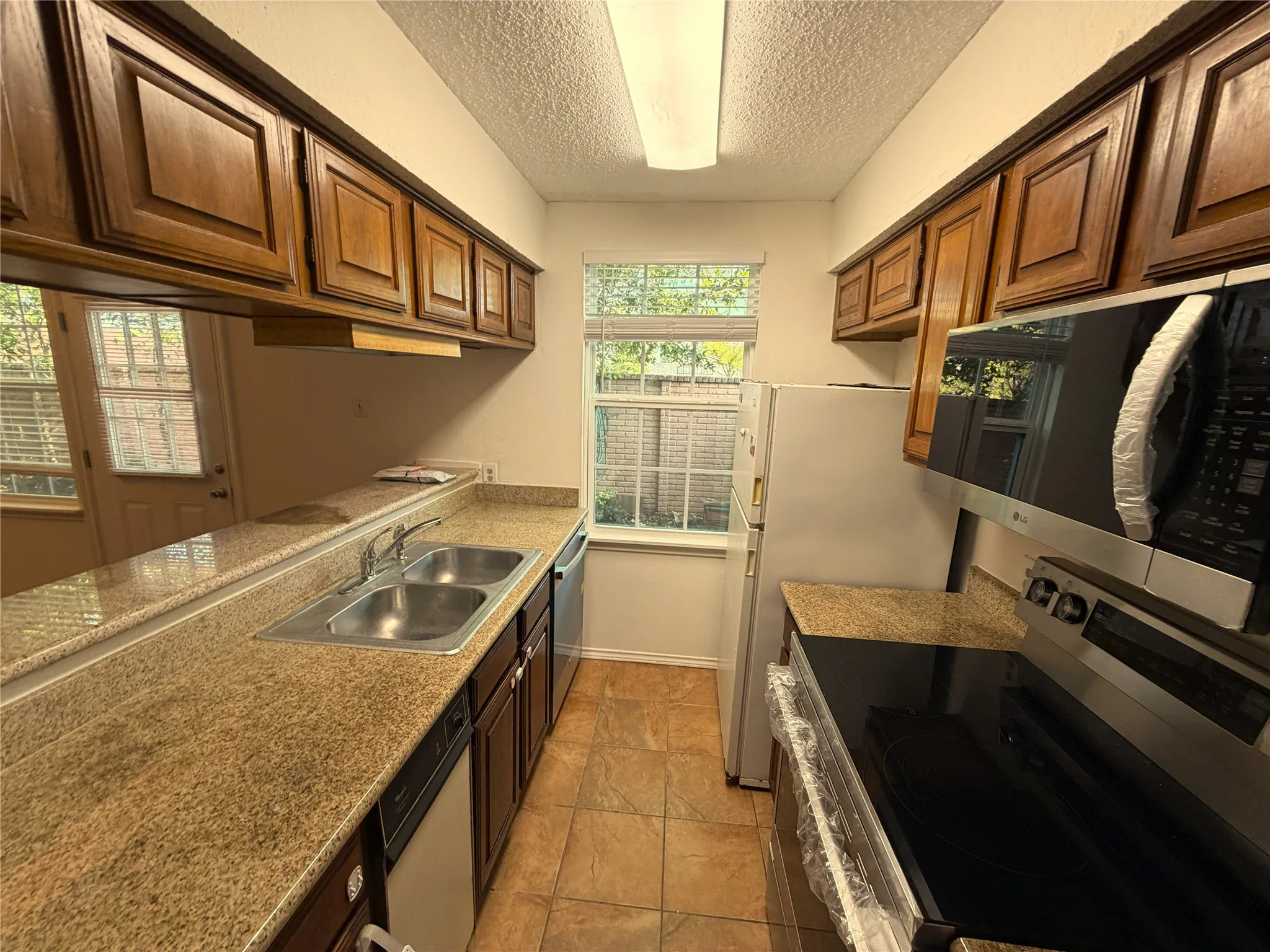 Galley kitchen featuring wood cabinetry, granite-finish countertops, and stainless steel appliances