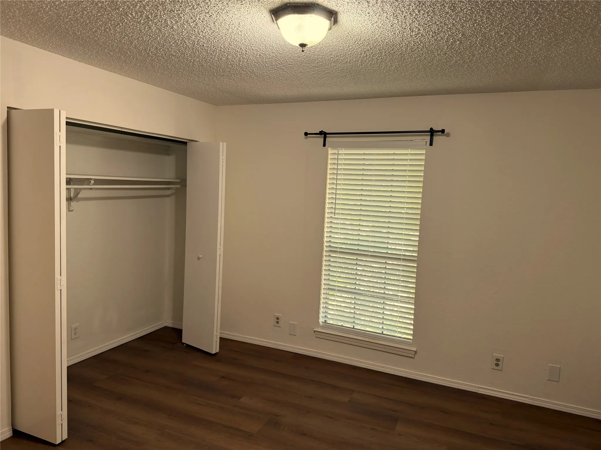 Room featuring wood-finish flooring, white walls, and a window with blinds