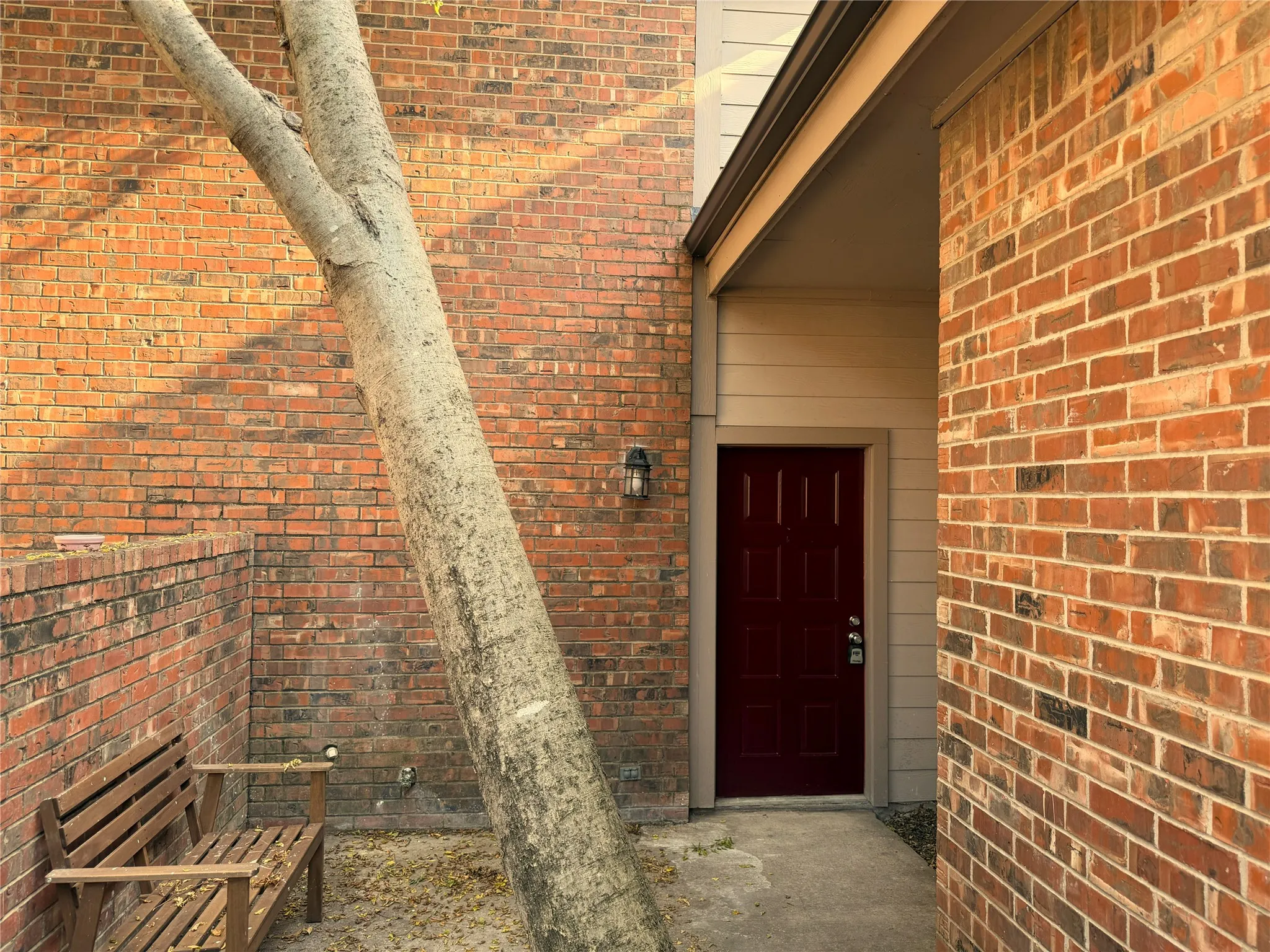 Brick exterior featuring a covered entry with a deep red paneled door and an exterior wall lantern
