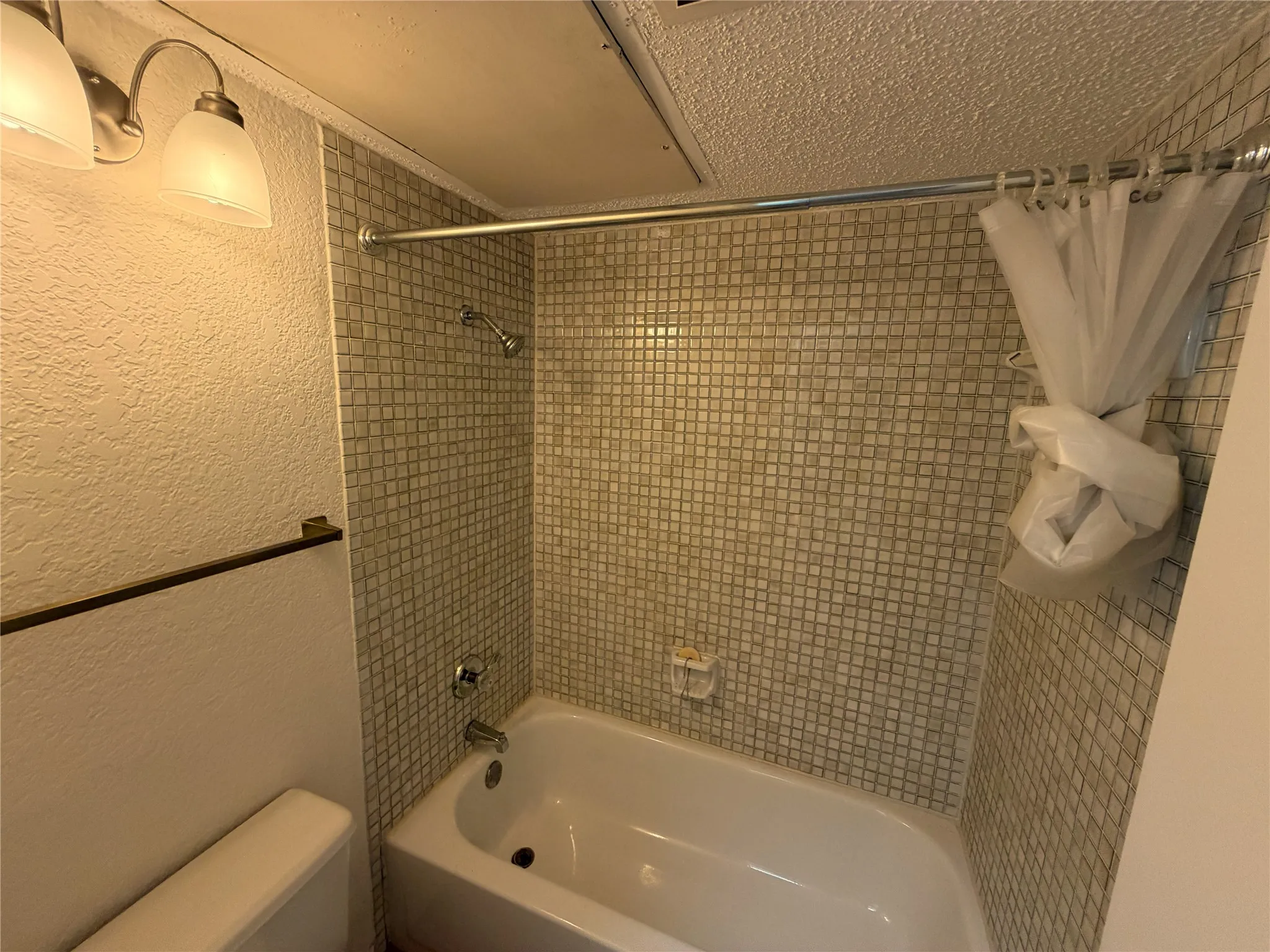Bathroom featuring a tiled shower surround, integrated bathtub, and a modern light fixture with frosted glass shades