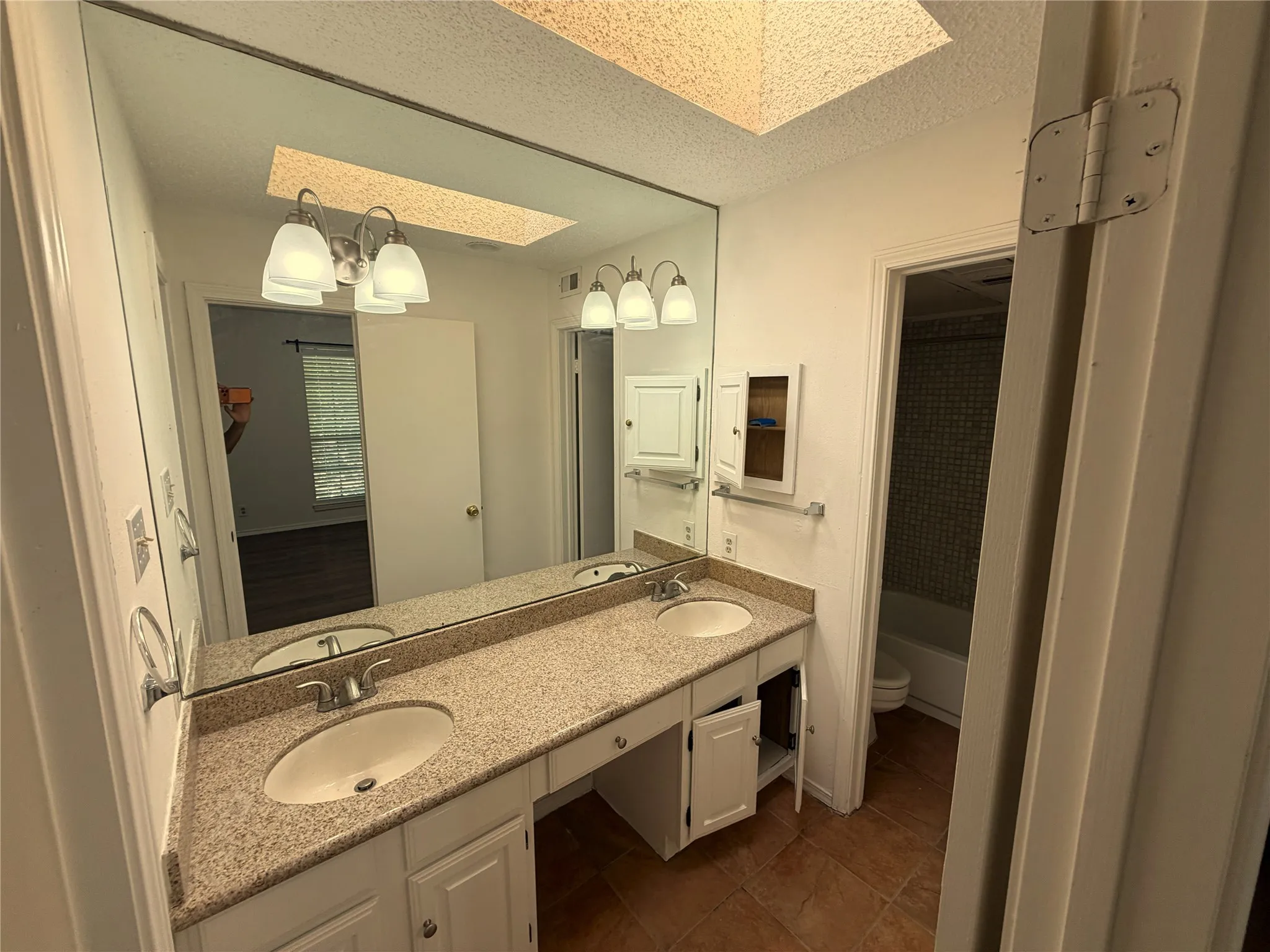 Dual sink vanity with a speckled countertop, a large wall-mounted mirror, and white cabinetry