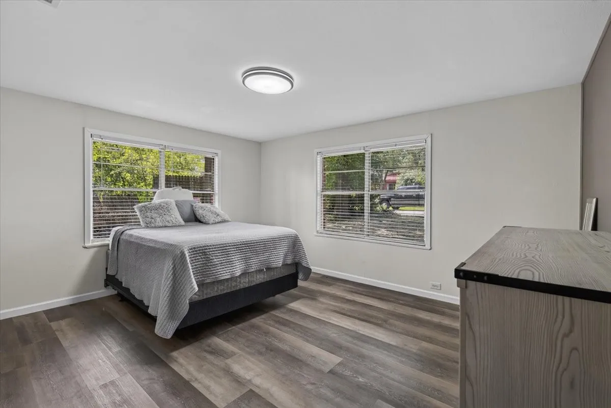 Room featuring wood-finish flooring, two large windows with blinds, light gray walls, white baseboards, and a flush-mount ceiling light fixture