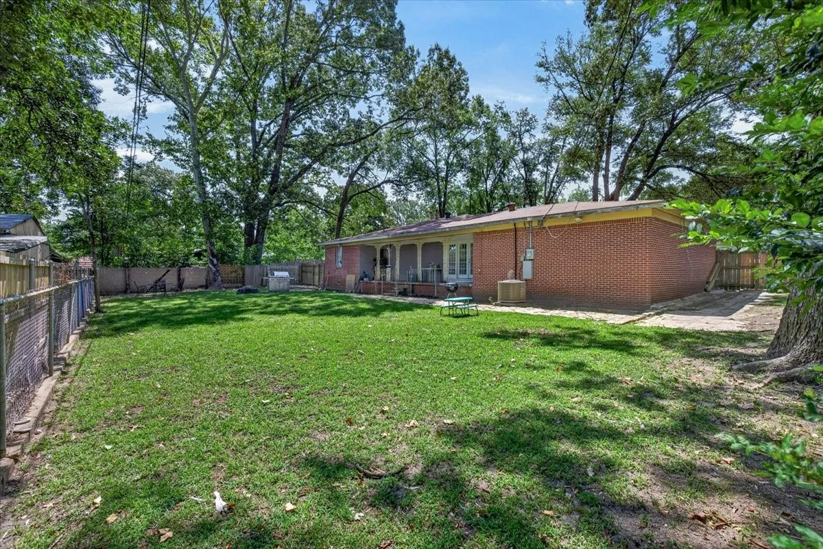 Expansive backyard featuring a manicured lawn, established shade trees, and a red brick exterior