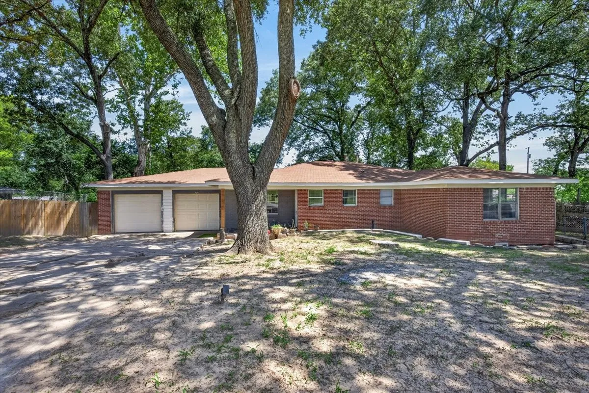 Brick exterior residence featuring a two-car garage, mature trees, and a partially fenced perimeter