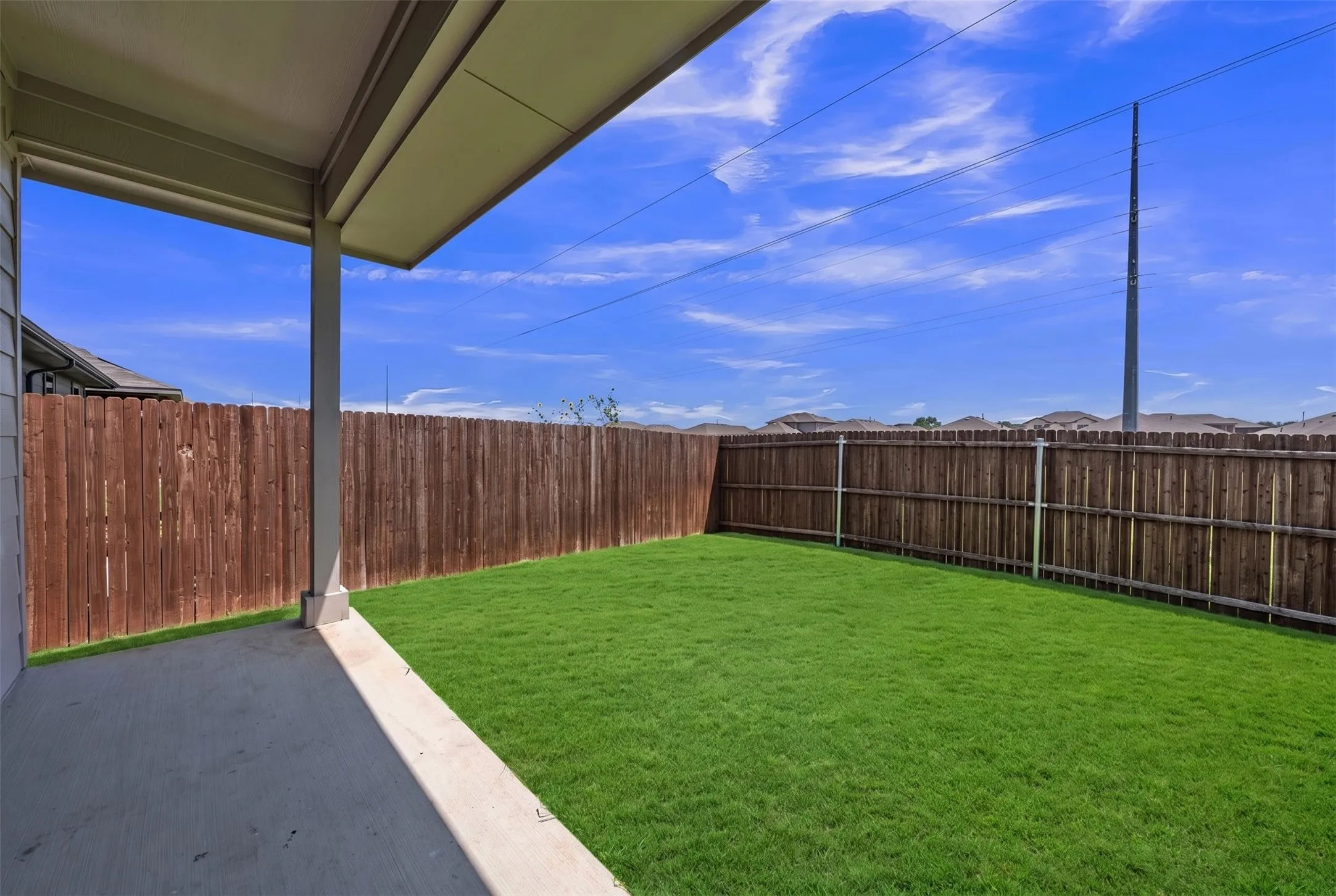 Expansive fenced backyard featuring a covered concrete patio, lush green lawn, and substantial wood privacy fencing