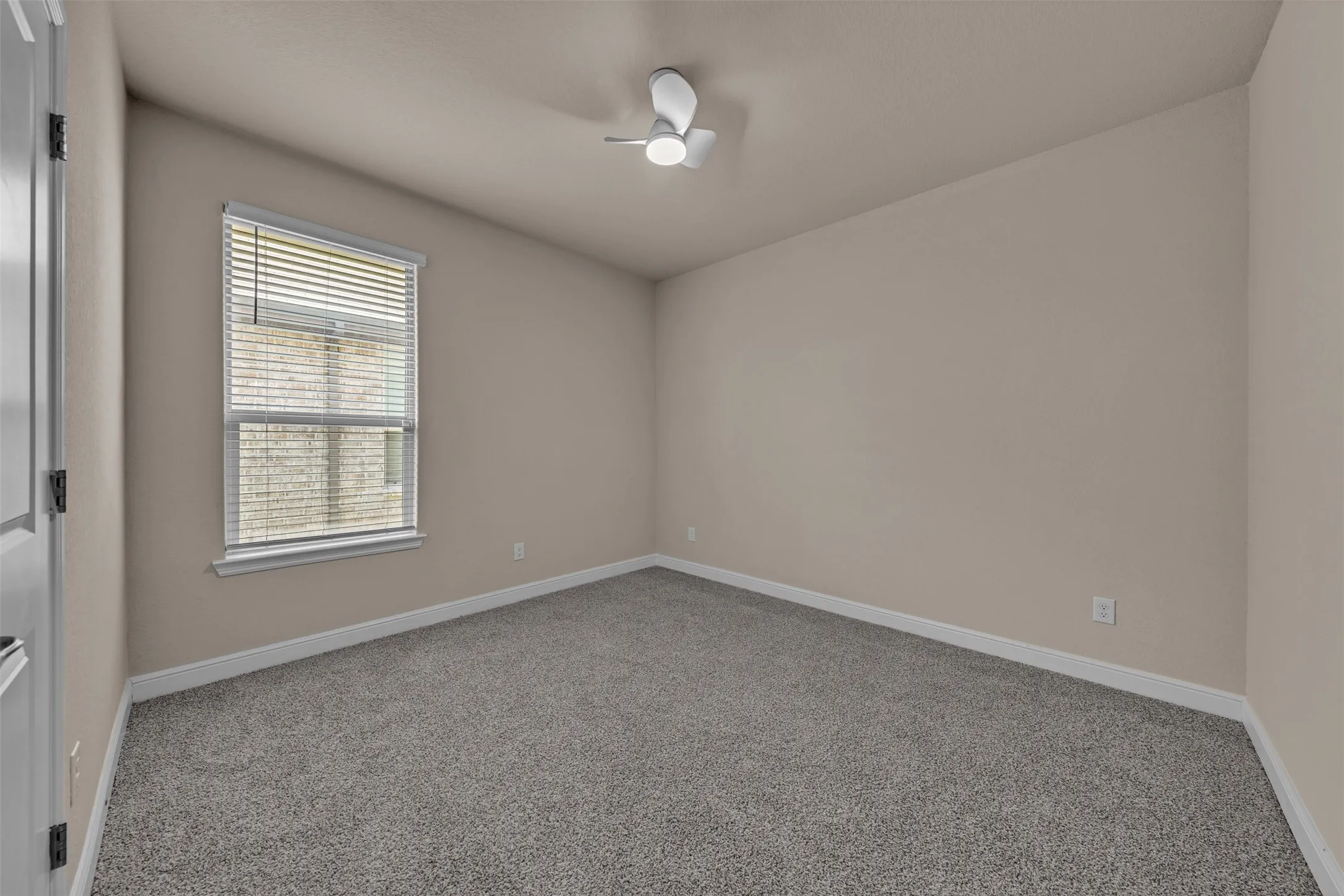 Neutral-toned room featuring light gray carpet, a contemporary ceiling fan, and a single window with horizontal blinds