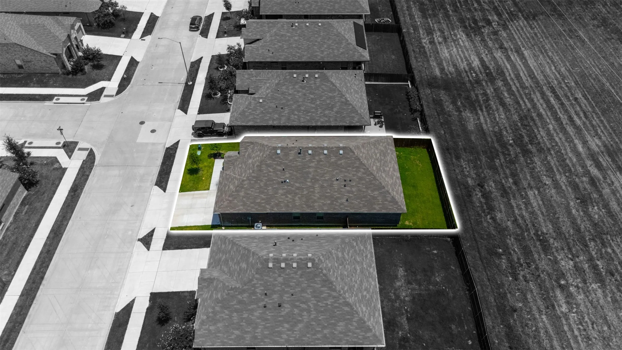 Aerial perspective highlighting a single-story residence with a dark shingle roof, a manicured green lawn, and concrete driveway