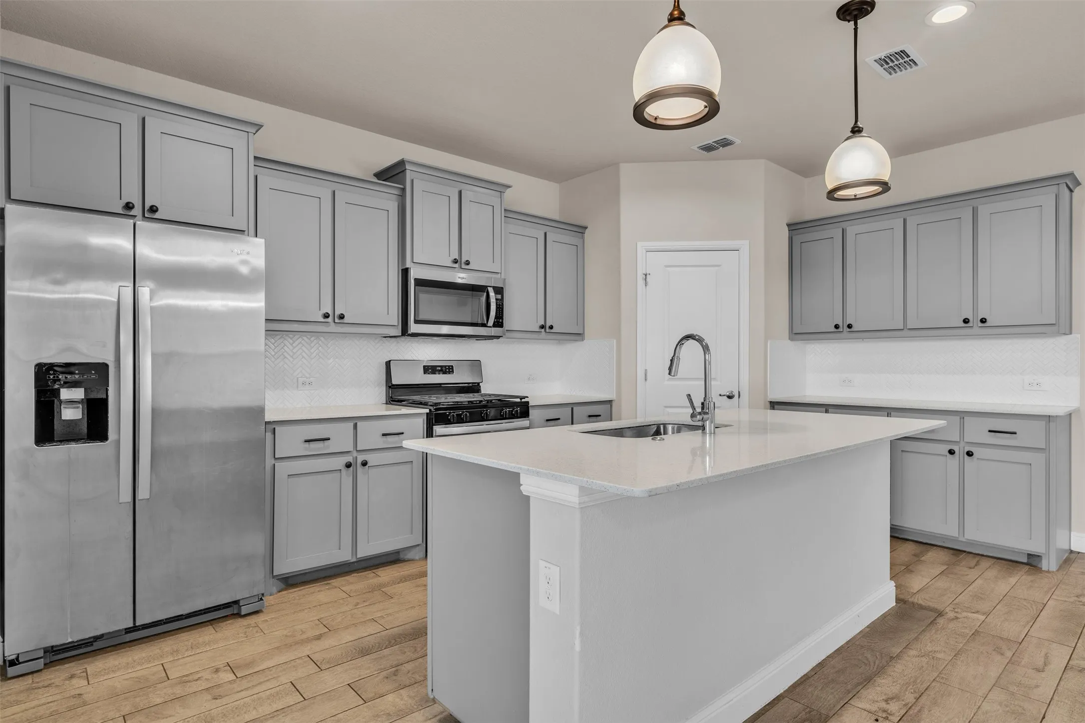 Modern kitchen featuring gray shaker-style cabinetry with black hardware, stainless steel appliances, and a central island with an undermount sink