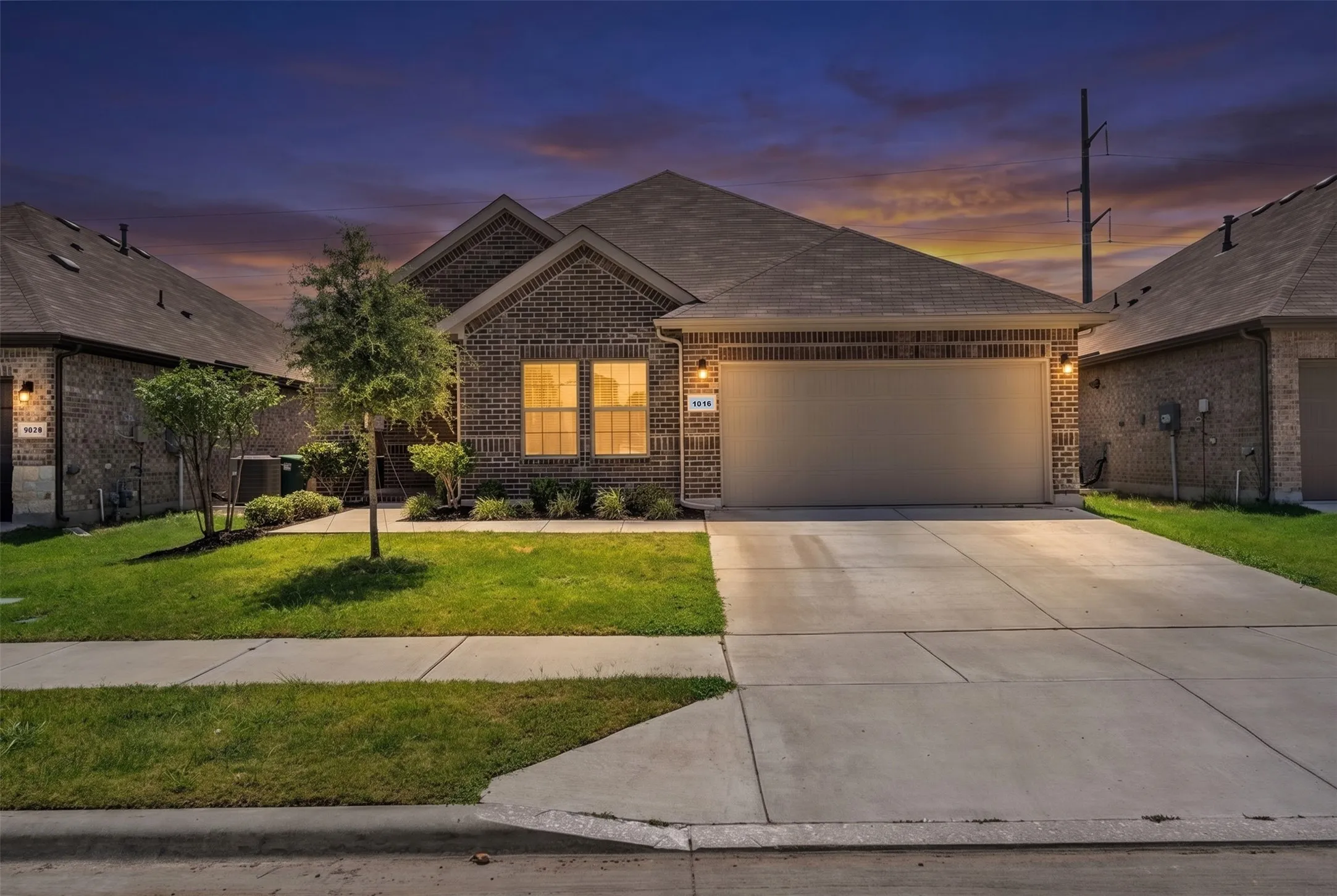 Brick facade home featuring a two-car garage, concrete driveway, and front lawn with mature landscaping