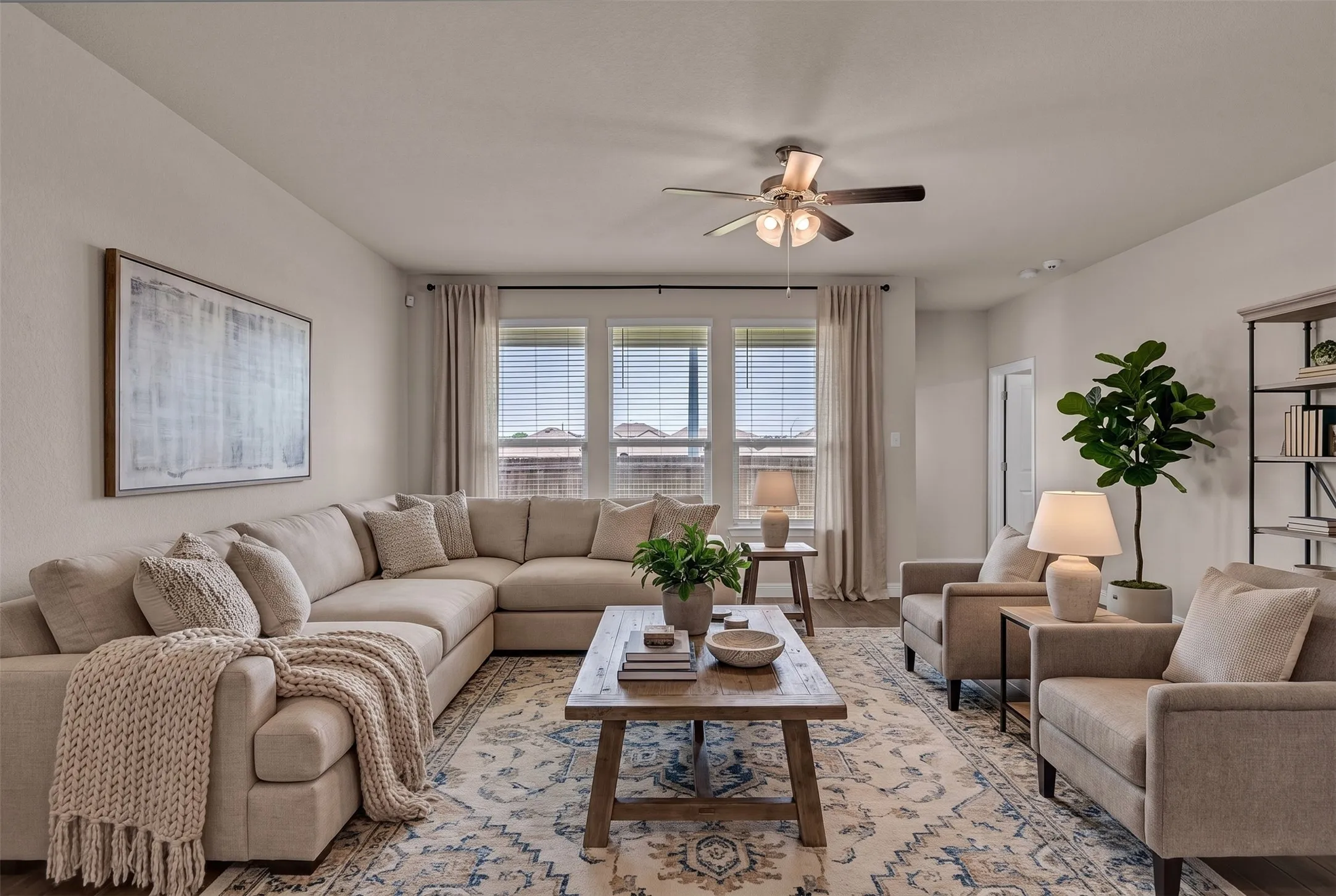Spacious living area featuring light neutral wall paint, wood-finish flooring, and a ceiling fan with integrated lighting