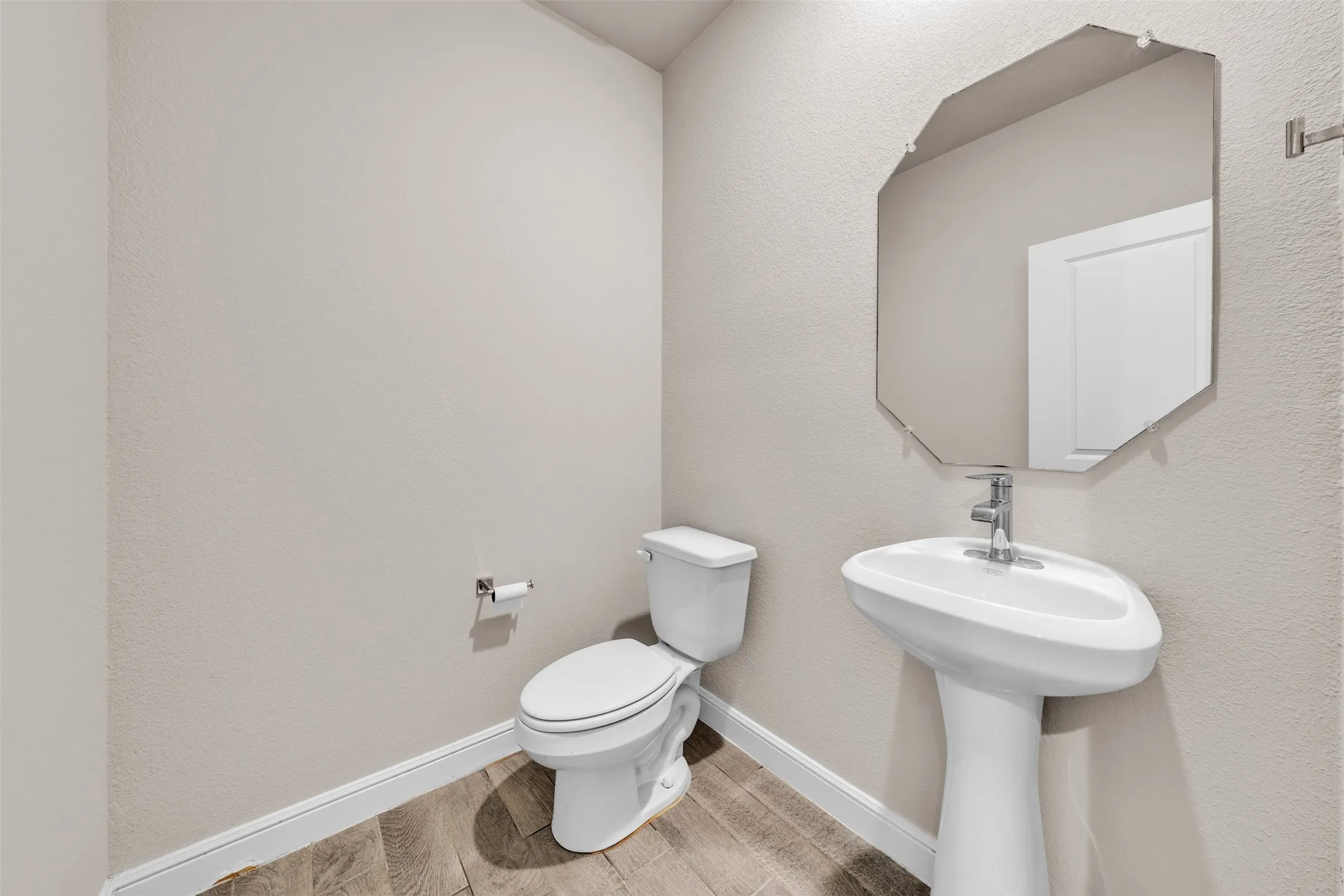 Pedestal sink with chrome faucet and an octagonal frameless mirror
