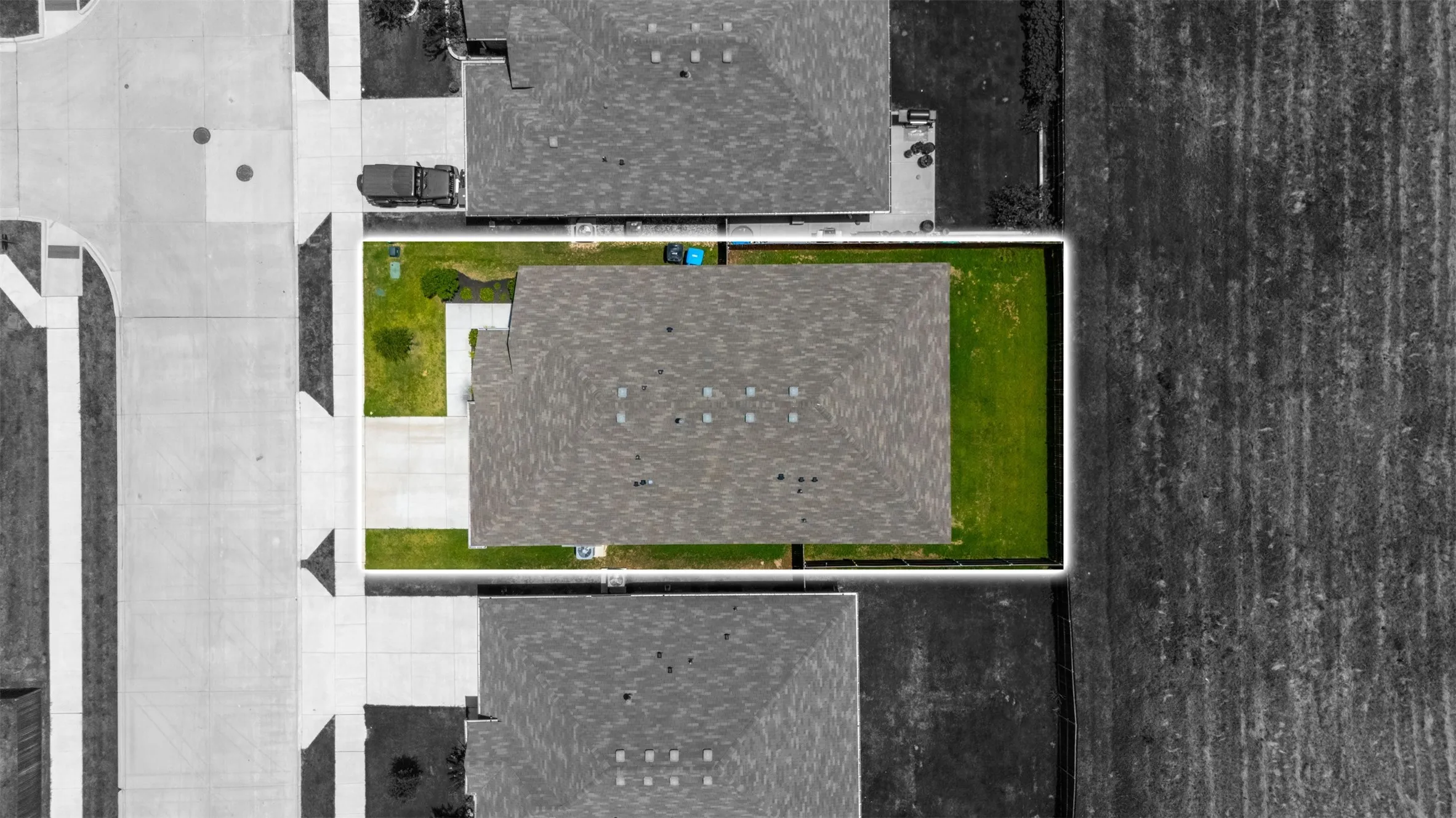 Aerial property overview featuring a shingle roof, concrete driveway, and surrounding green lawn