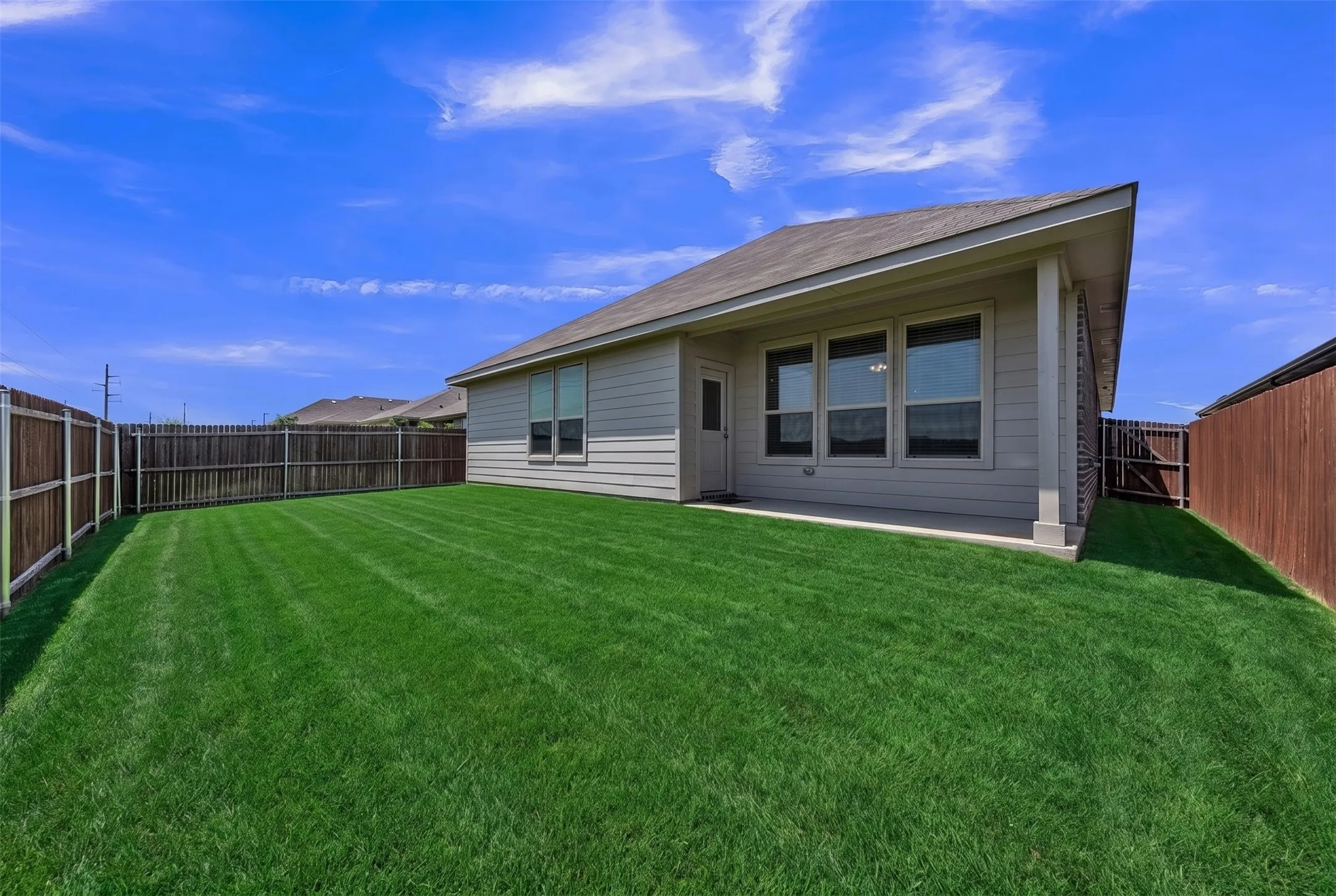Expansive backyard featuring a manicured lawn, full perimeter privacy fencing, covered patio, and multiple windows