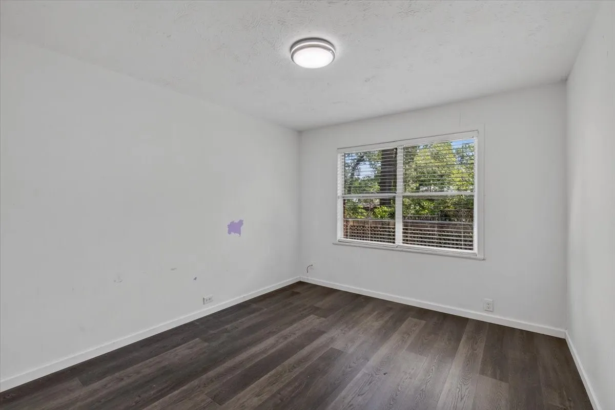 Room featuring wood-finish flooring, white baseboards, a white ceiling with a flush-mount light fixture, and a window with horizontal blinds