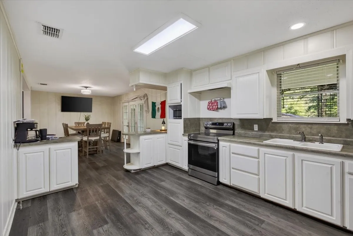 Open-concept kitchen featuring wood-finish flooring, white cabinetry, a built-in microwave, and a stainless steel range