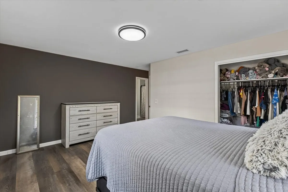 Bedroom featuring rich wood-finish flooring, a contemporary flush-mount ceiling light, and a built-in closet with hanging rods and shelf storage