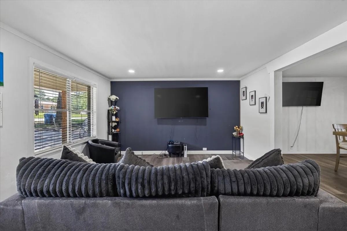 Open-concept living space featuring wood-finish flooring, recessed lighting, and a prominent accent wall