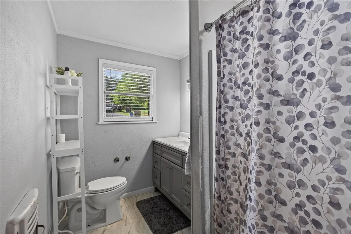 Bathroom featuring a window with blinds, a toilet, a vanity with a countertop and sink, and a shower area with a shower curtain