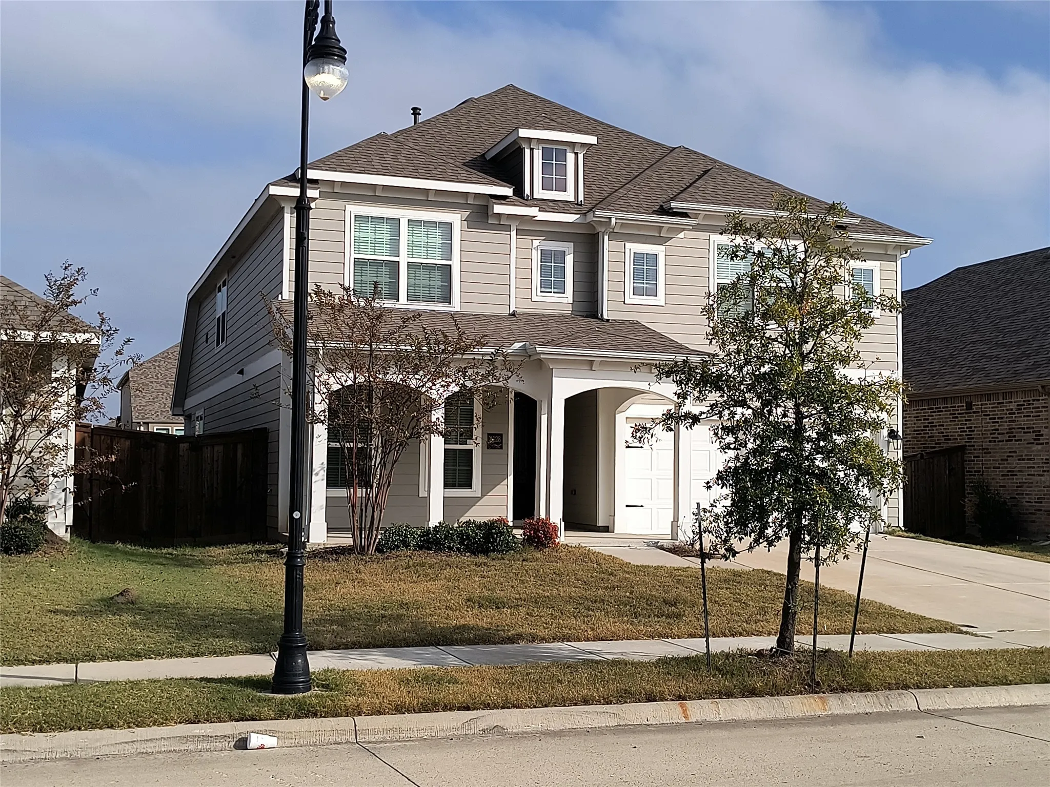 Two-story residence featuring light gray siding with white trim, a brown shingle roof, and an integrated two-car garage