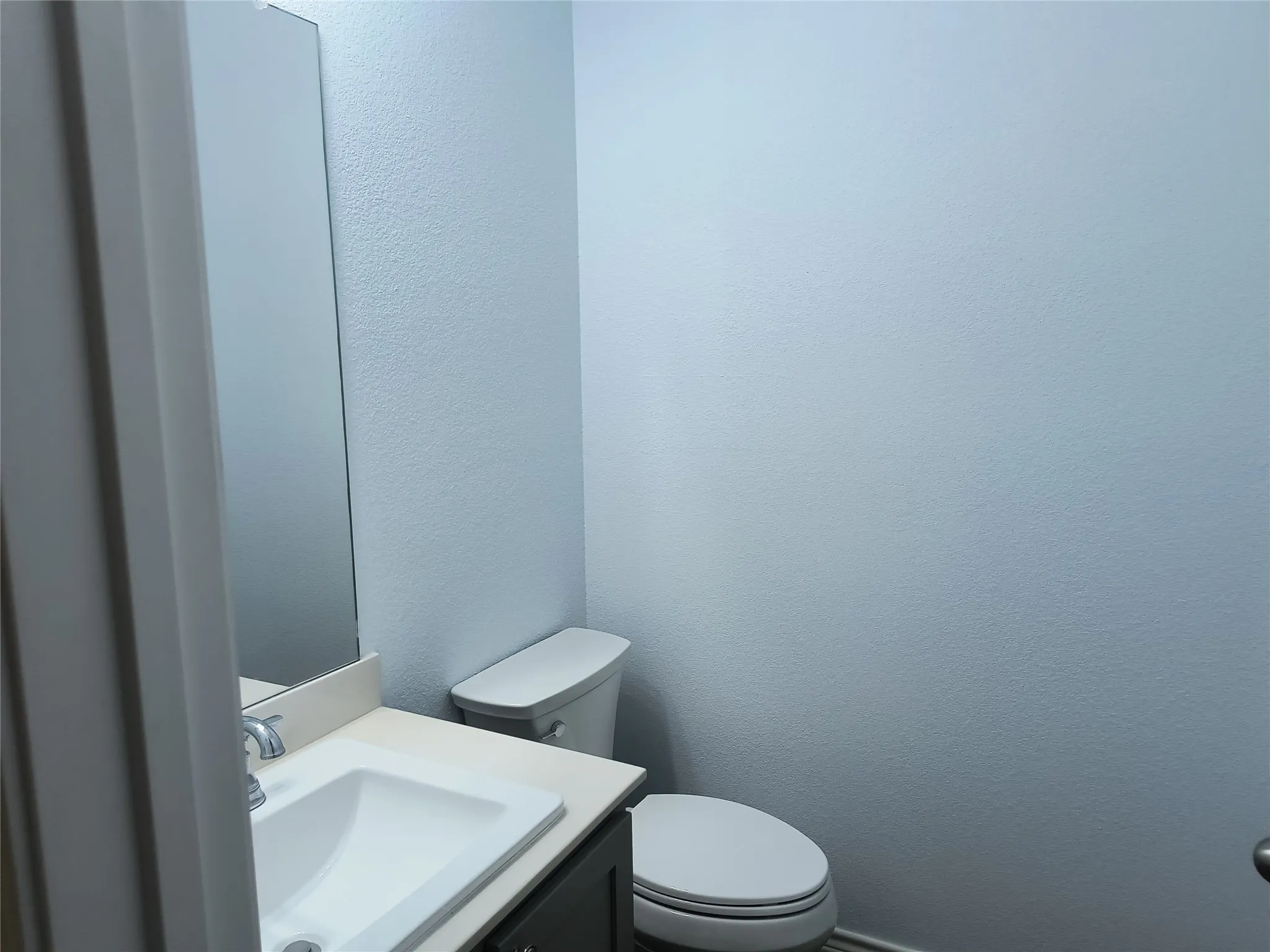 Bathroom featuring a white toilet, dark wood-finish vanity with an integrated sink, polished chrome faucet, and a wall-mounted mirror