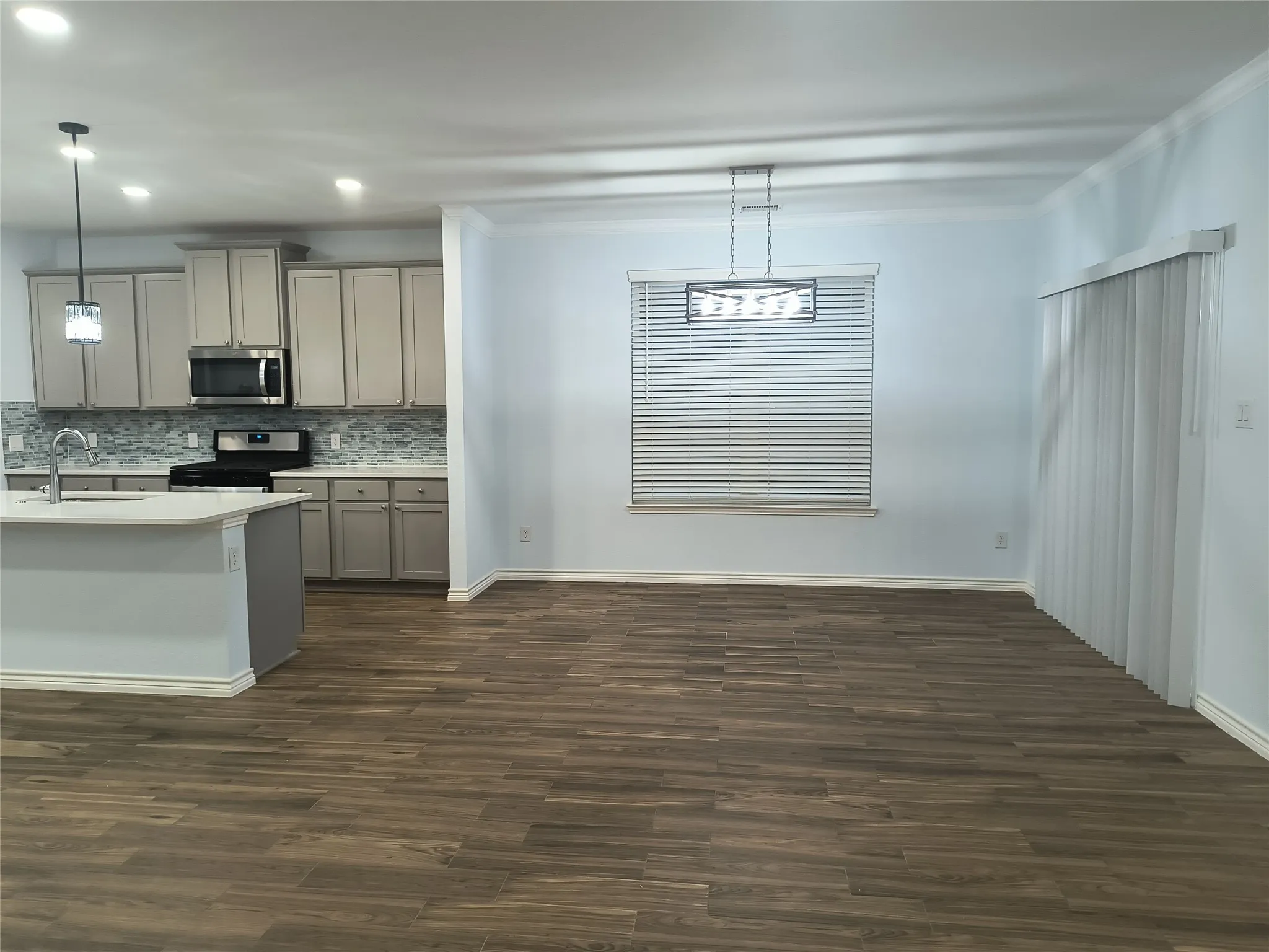 Open-concept living space featuring wood-finish flooring, a kitchen island with a single-basin sink, light-toned cabinetry, stainless steel appliances, and a tiled backsplash
