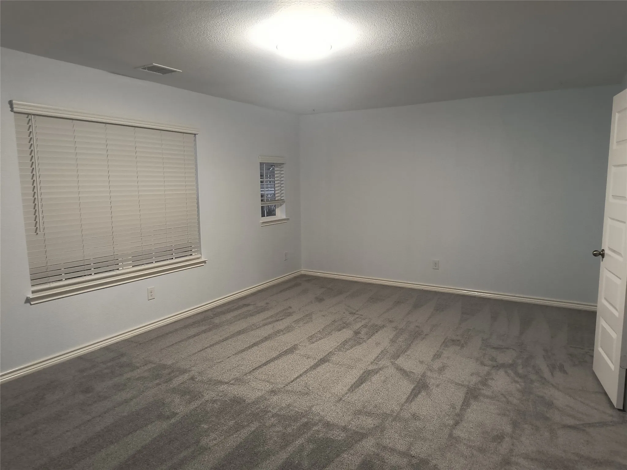 Spacious room featuring gray wall-to-wall carpeting, light-colored walls, and white trim