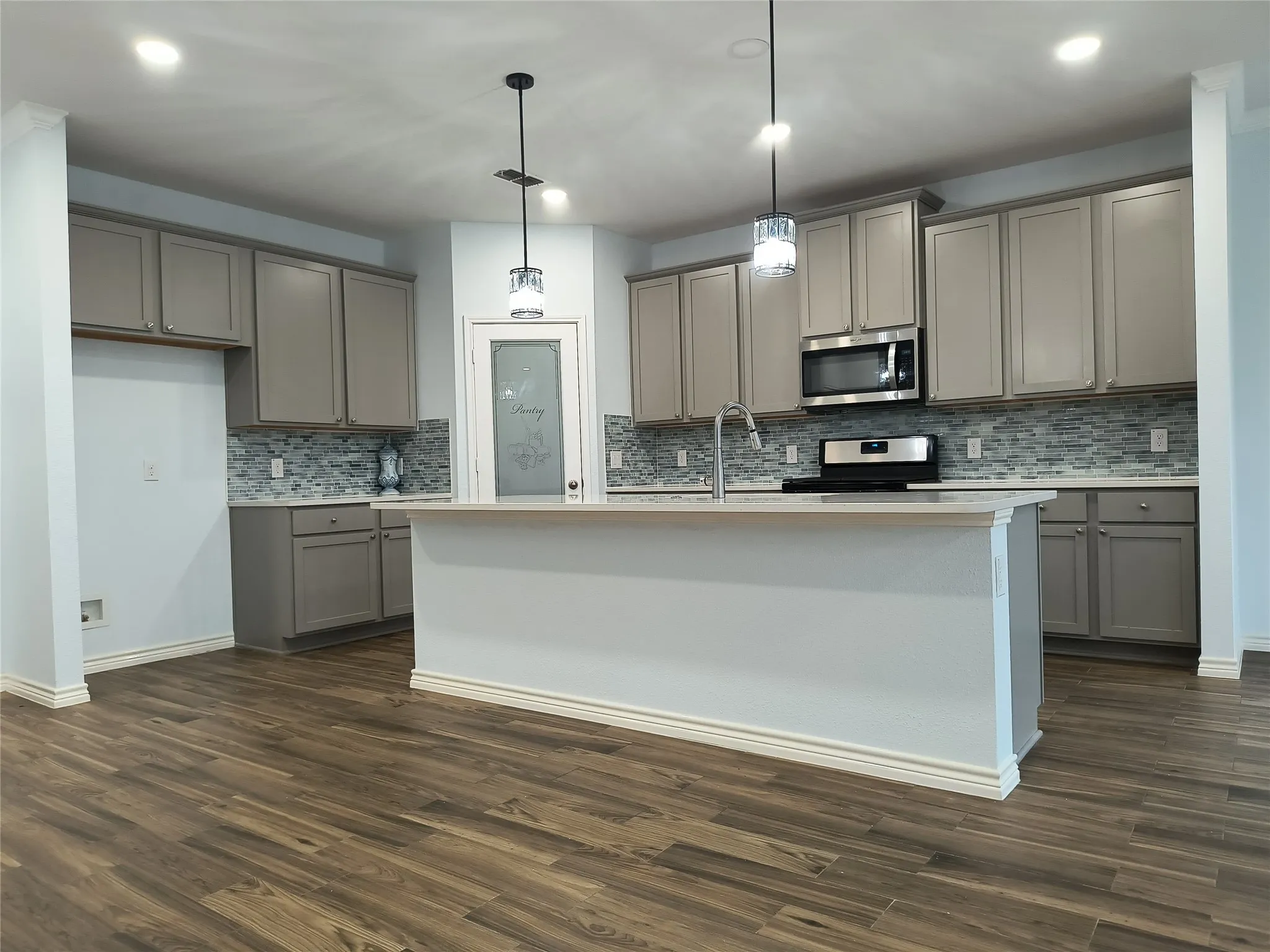 Kitchen featuring wood-finish flooring, a central island, grey cabinetry, a mosaic tile backsplash, and stainless steel appliances including a microwave and range
