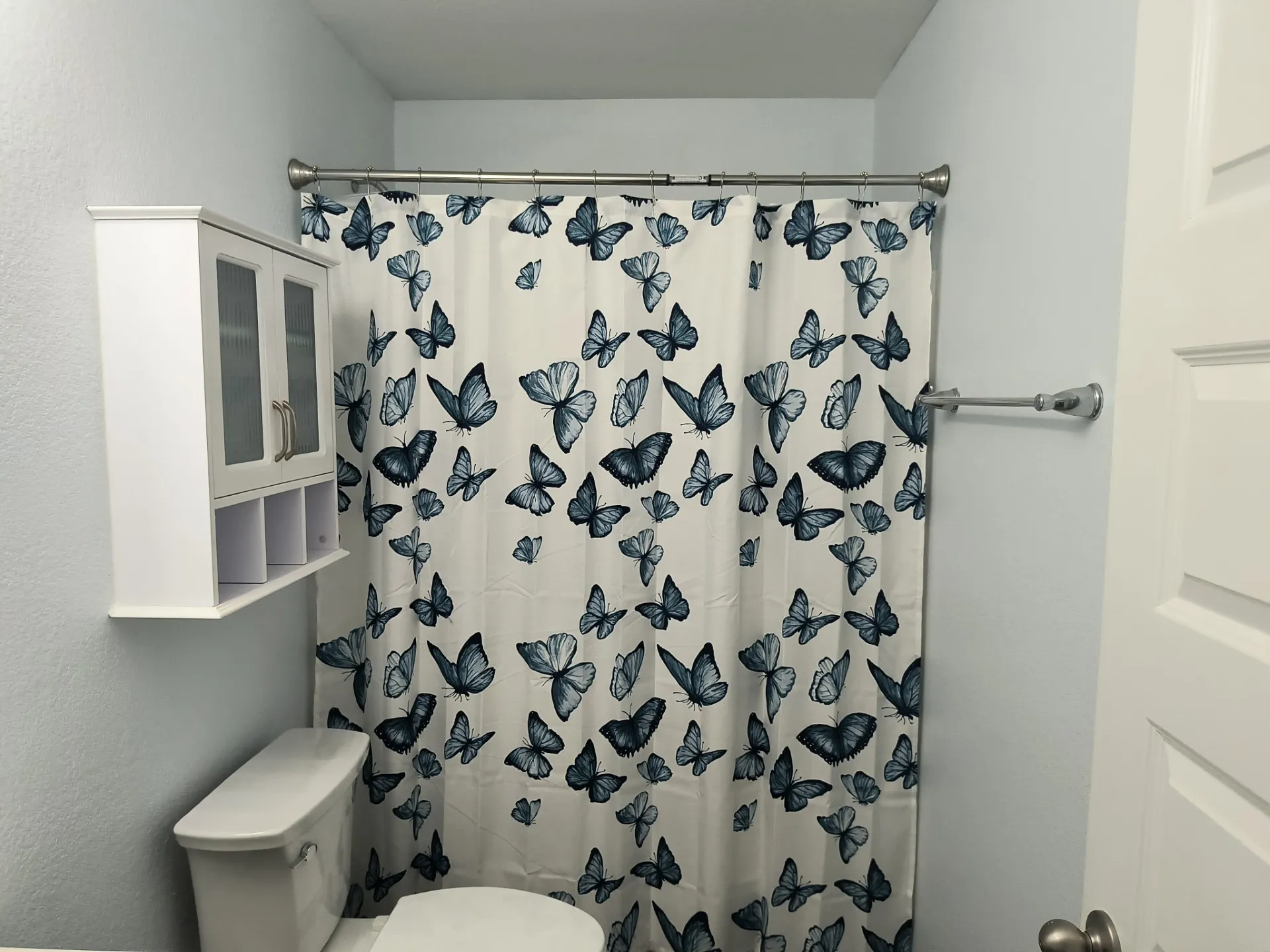 Bathroom featuring a wall-mounted cabinet with glass-front doors, open cubby storage, and a white toilet