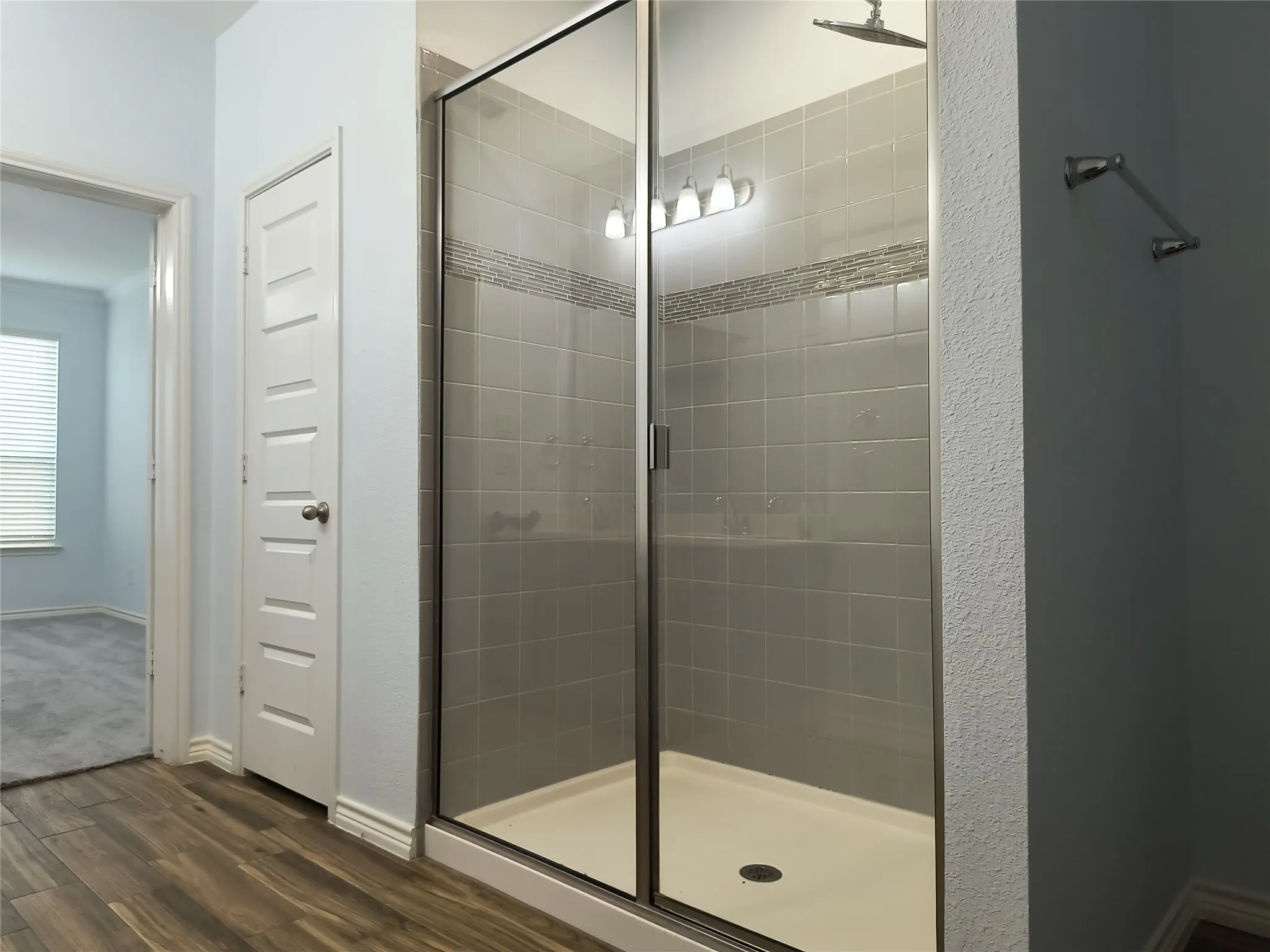 Spacious shower enclosure with glass doors, contemporary gray tile surround, decorative accent tile band, and overhead shower fixture