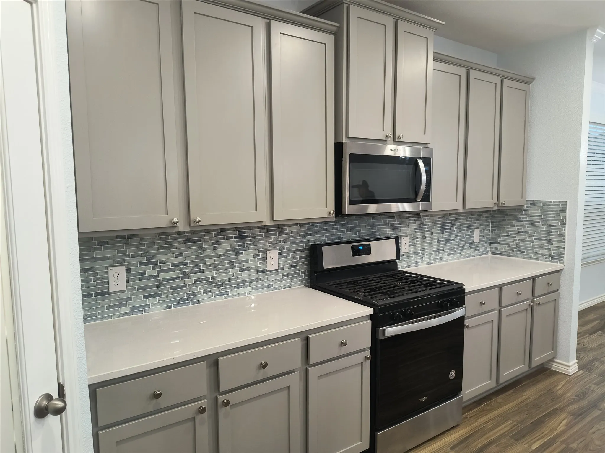 Kitchen featuring wood-finish flooring, a central island, grey cabinetry, a mosaic tile backsplash, and stainless steel appliances including a microwave and range